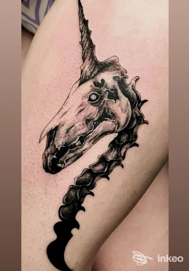 Tatuaggio nero su coscia raffigurante una testa scheletrica con corno e colonna stilizzata, foto fornita da KINK tattoo studio, Biella.