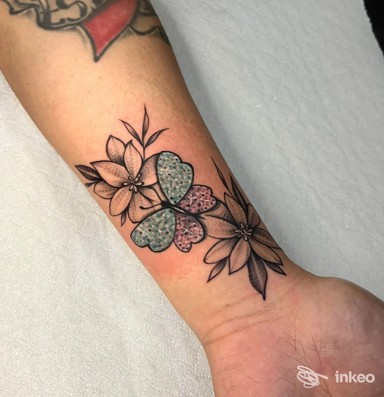 Tatuaggio floreale sull'avambraccio con trifoglio puntinato e fiori lineari, realizzato da Keka Permanent a Torino.