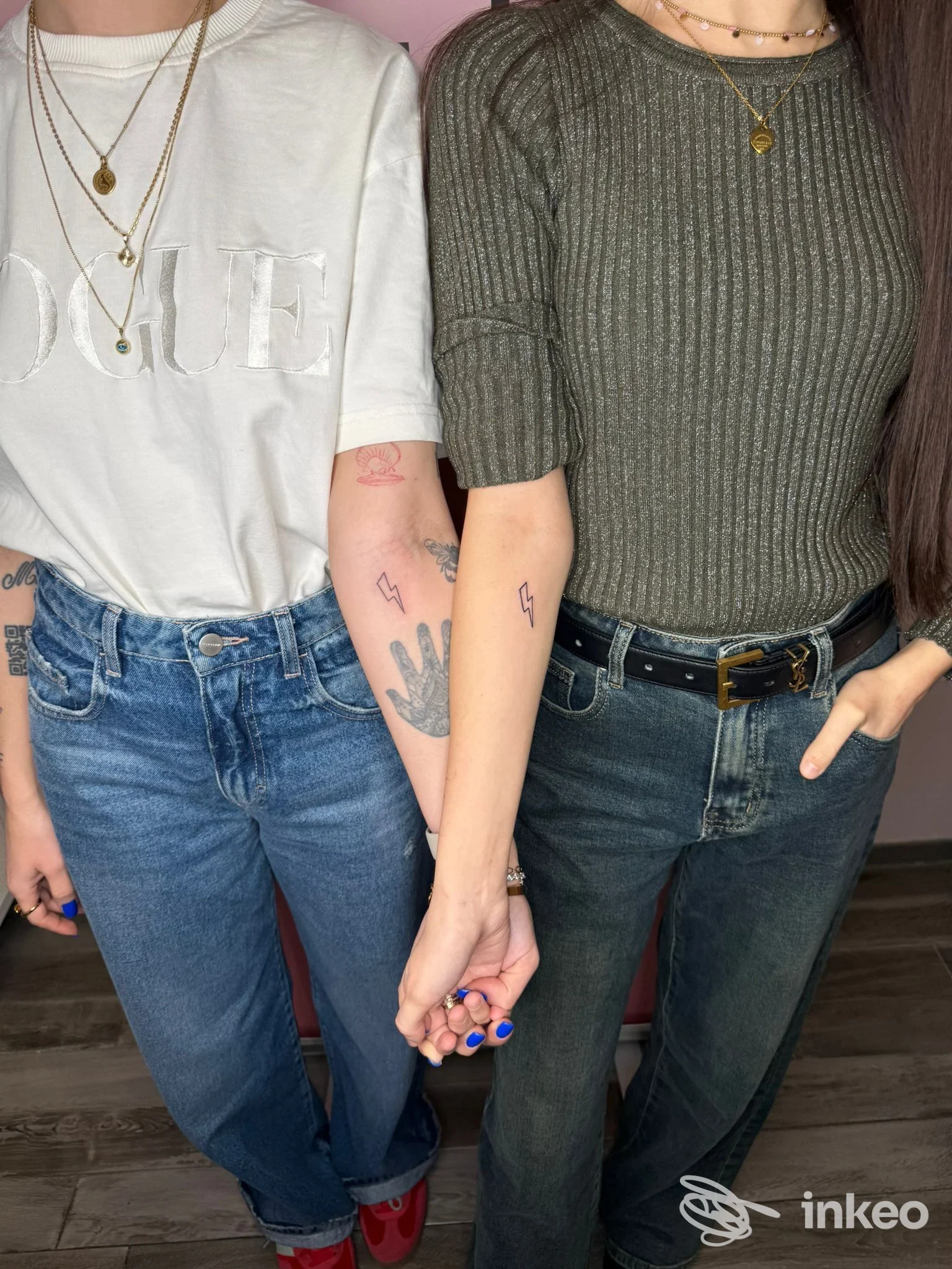 Due persone mano nella mano che mostrano piccoli tatuaggi a fulmine e altri disegni su avambracci e polso. Keka Permanent, Torino.