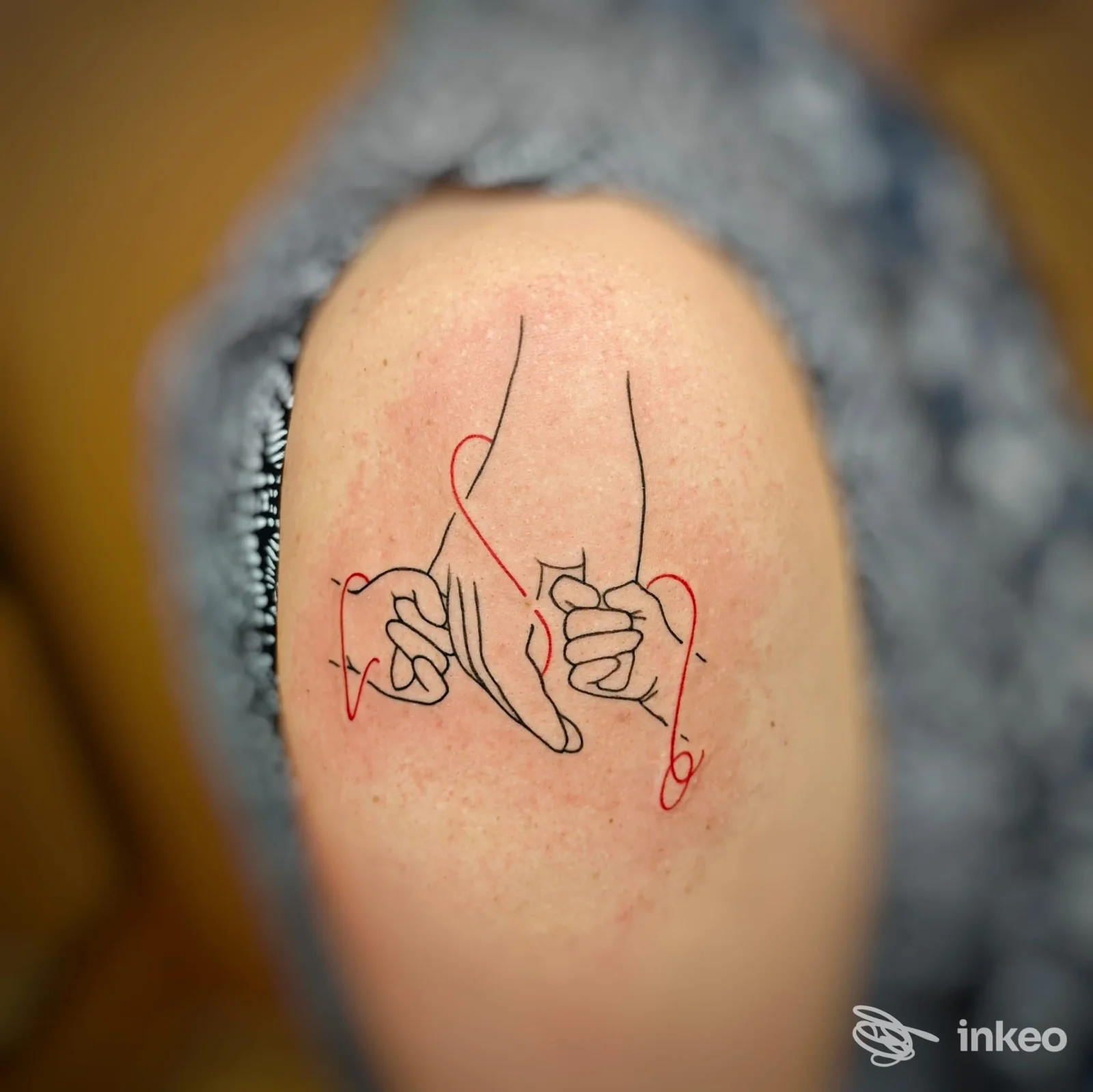Primo piano di un tatuaggio a linee sottili con dettagli rossi sul deltoide; immagine fornita da M.R. TATTOO STUDIO, Canelli.