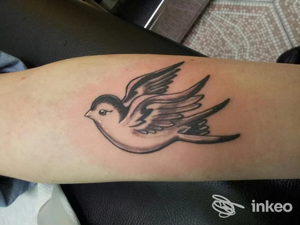 Tatuaggio a inchiostro nero raffigurante un uccello stilizzato sull'avambraccio, foto fornita da Madison Tattoo Torino, Torino.