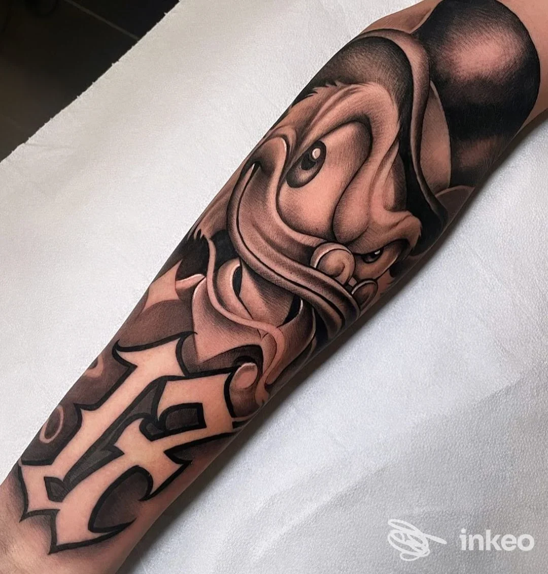 Tatuaggio black & grey su avambraccio con volto stilizzato e lettering, scatto del Malamanera Tattoo Shop a Nichelino.