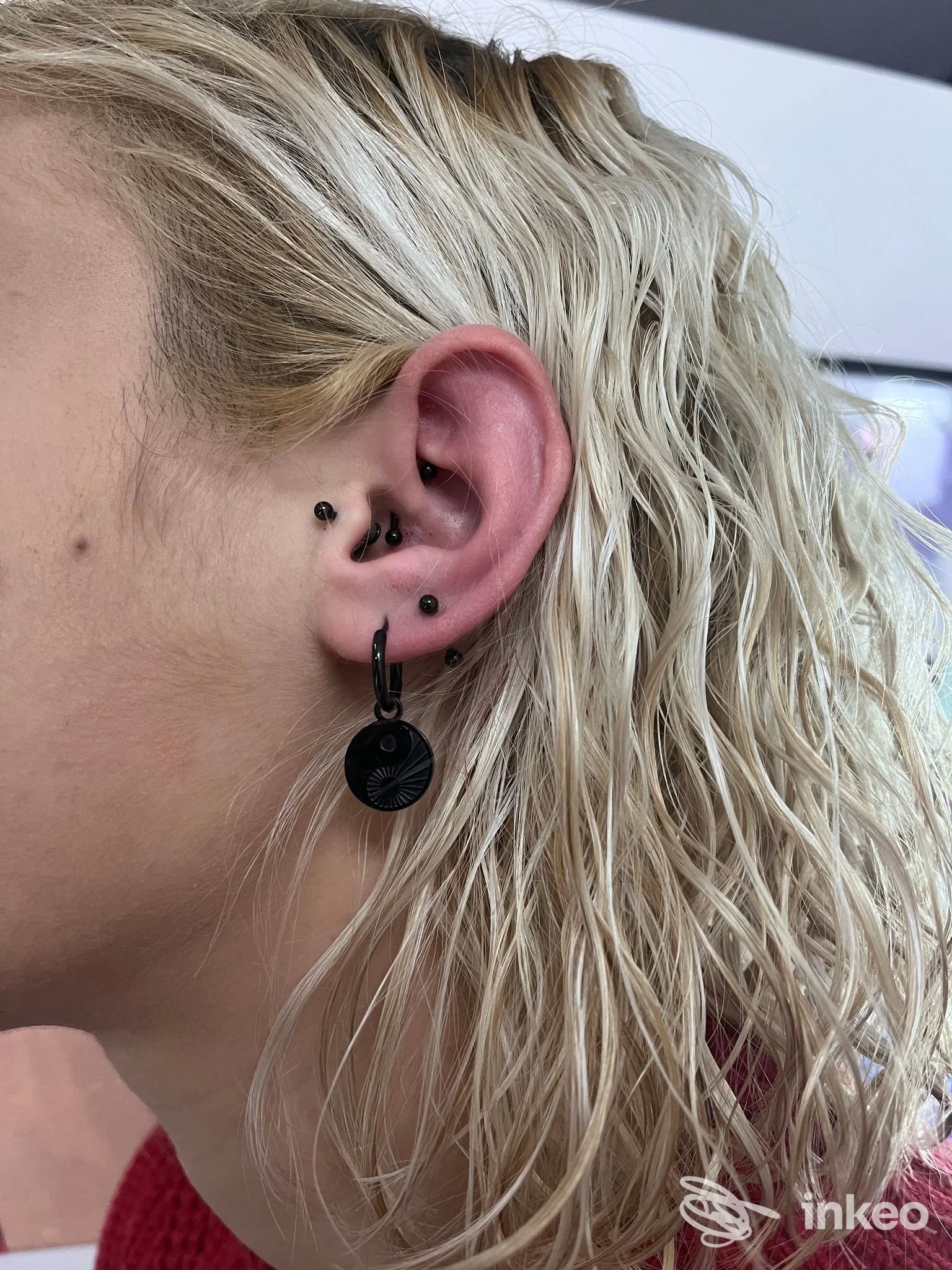 Primo piano di un orecchio con più piercing neri e un pendente, eseguiti da Maargotz Body Piercing a Domodossola.