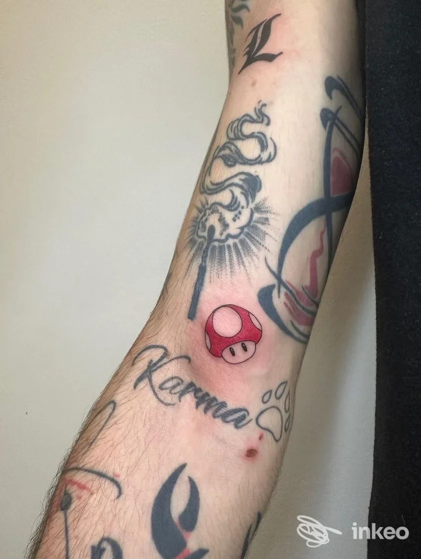 Avambraccio tatuato con un piccolo fungo rosso e bianco e scritte in corsivo, foto fornita da Nuni Piercink Lab, Torino.