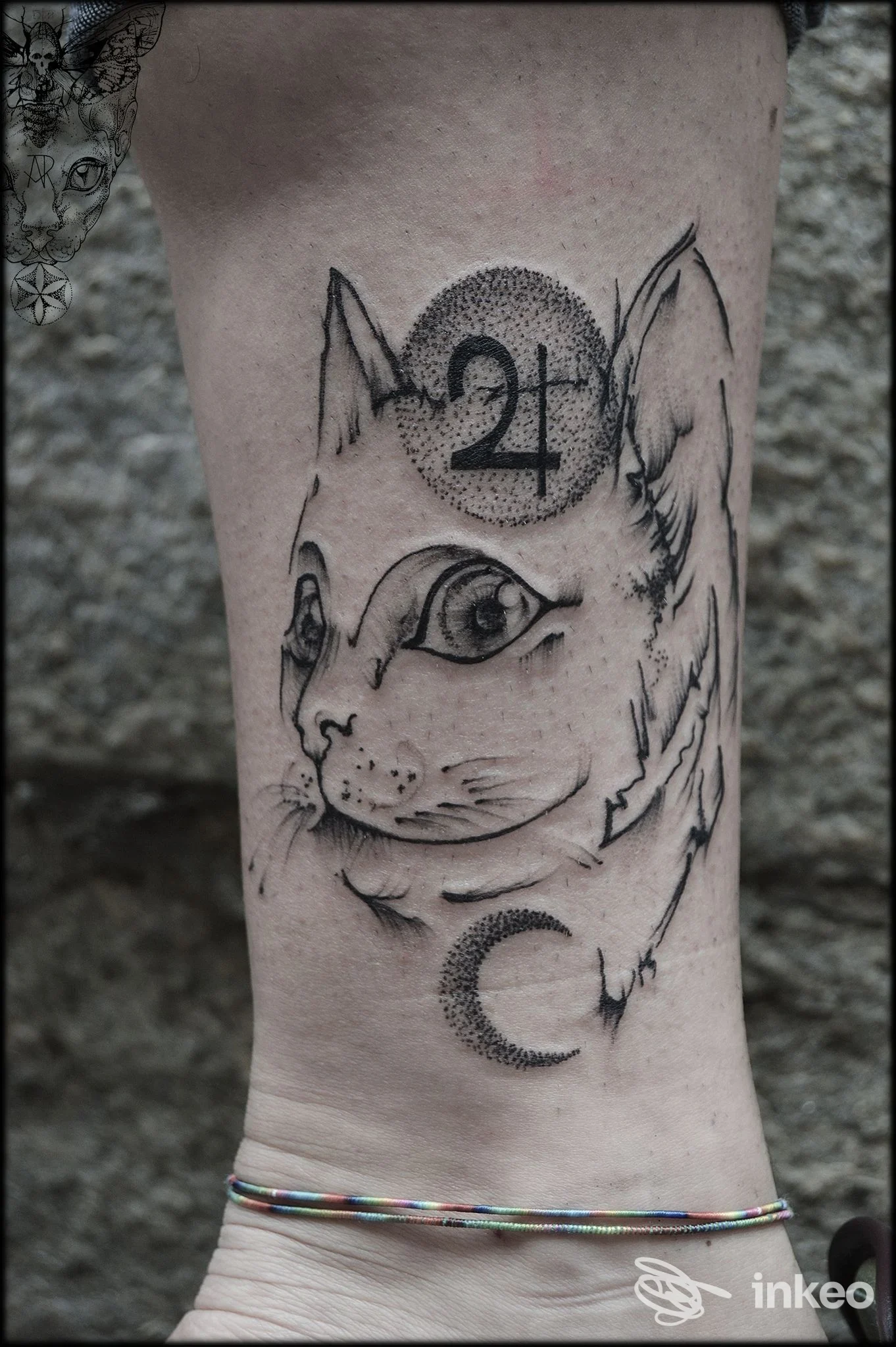 Primo piano di tatuaggio su caviglia raffigurante testa di gatto stilizzata e simboli in nero; Namaste Tattoo Studio - Anita Rossi, Torino.