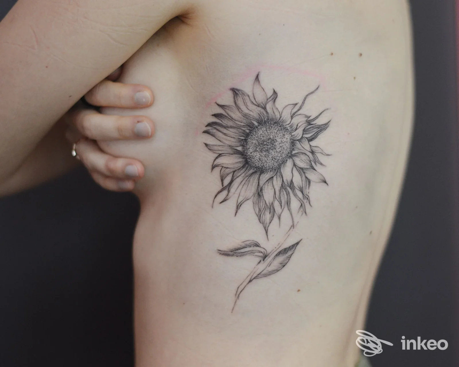 Tatuaggio a inchiostro nero di un girasole sul fianco sinistro; Namaste Tattoo Studio, Torino.