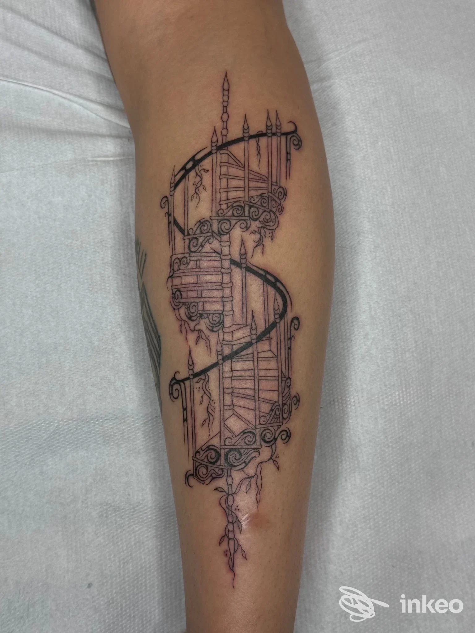 Tatuaggio a linee nere di una scala a chiocciola ornamentale sul polpaccio, Orme Tattoo Studio, Torino.
