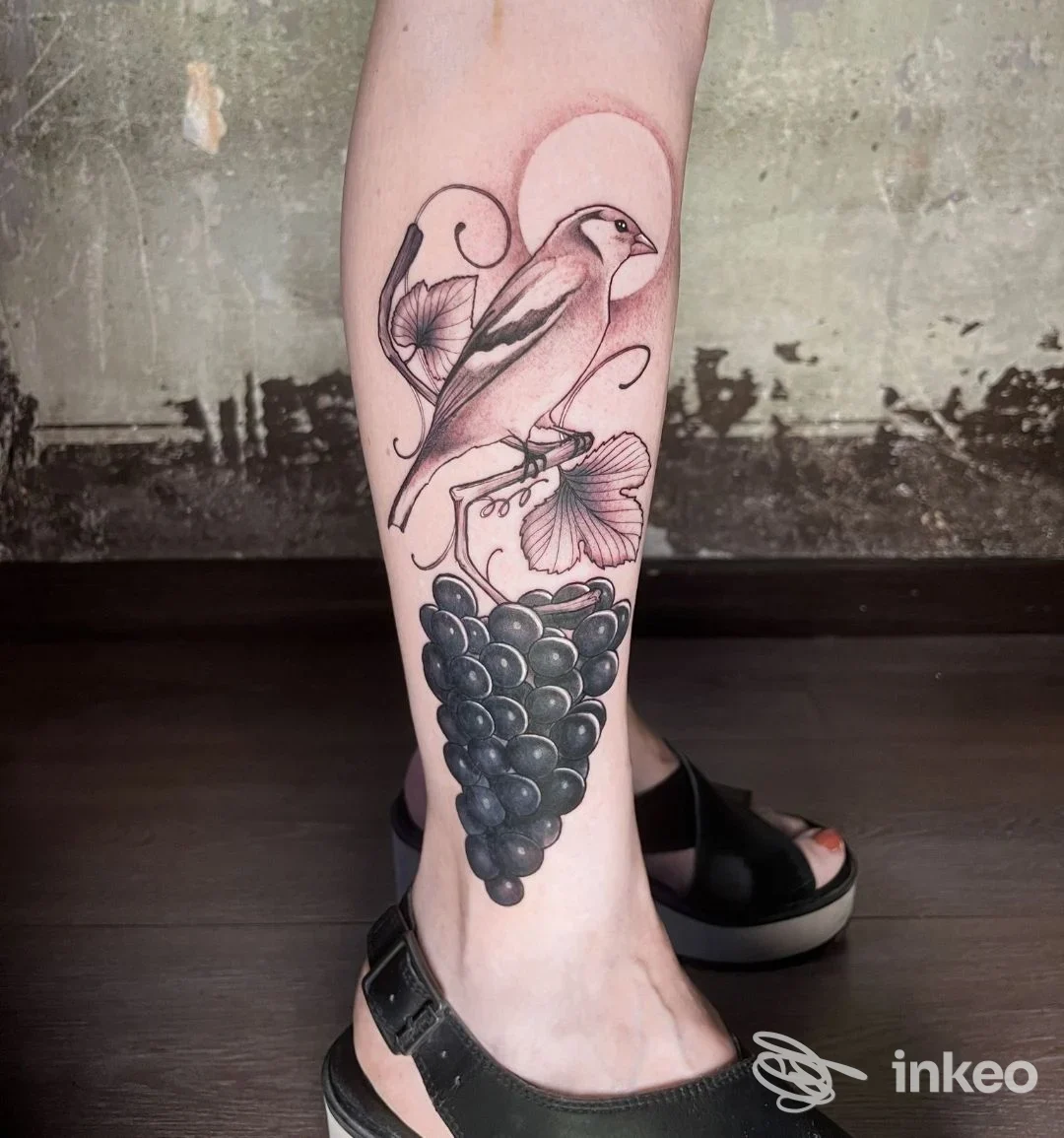 Tatuaggio su polpaccio raffigurante un uccello e un grappolo d'uva, fotografato presso Pig.Menti Tattoo Club a Torino.