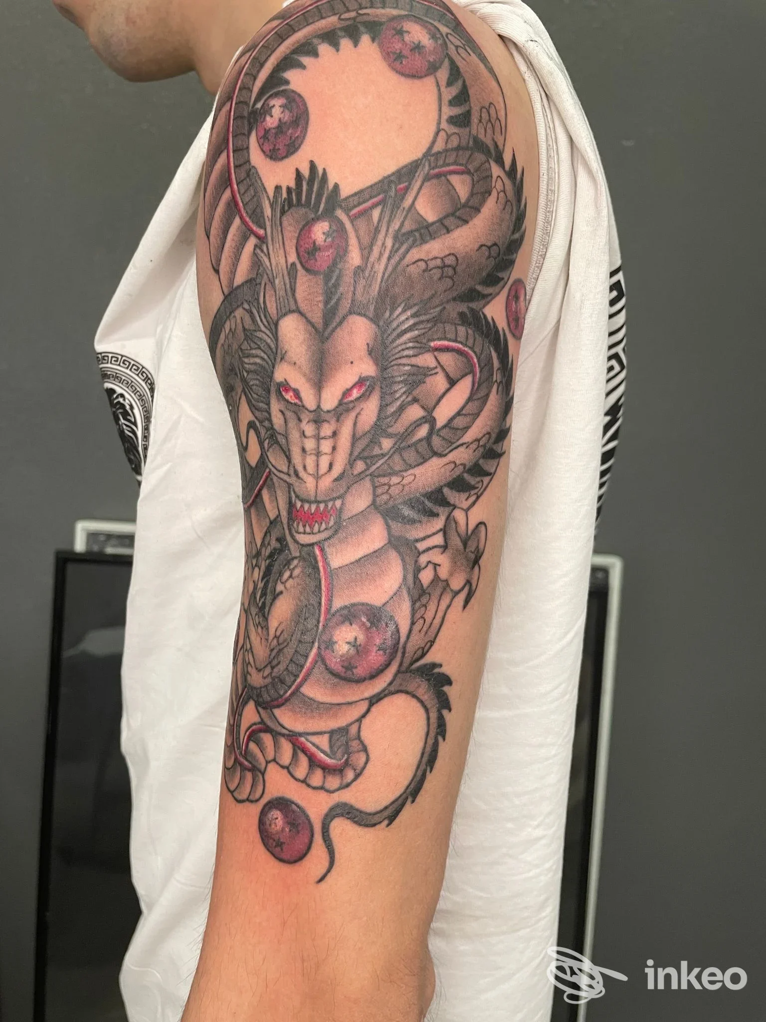 Braccio di una persona con un tatuaggio draconiforme e orbite rotonde rosse, visibile da spalle al gomito, su pelle reale.