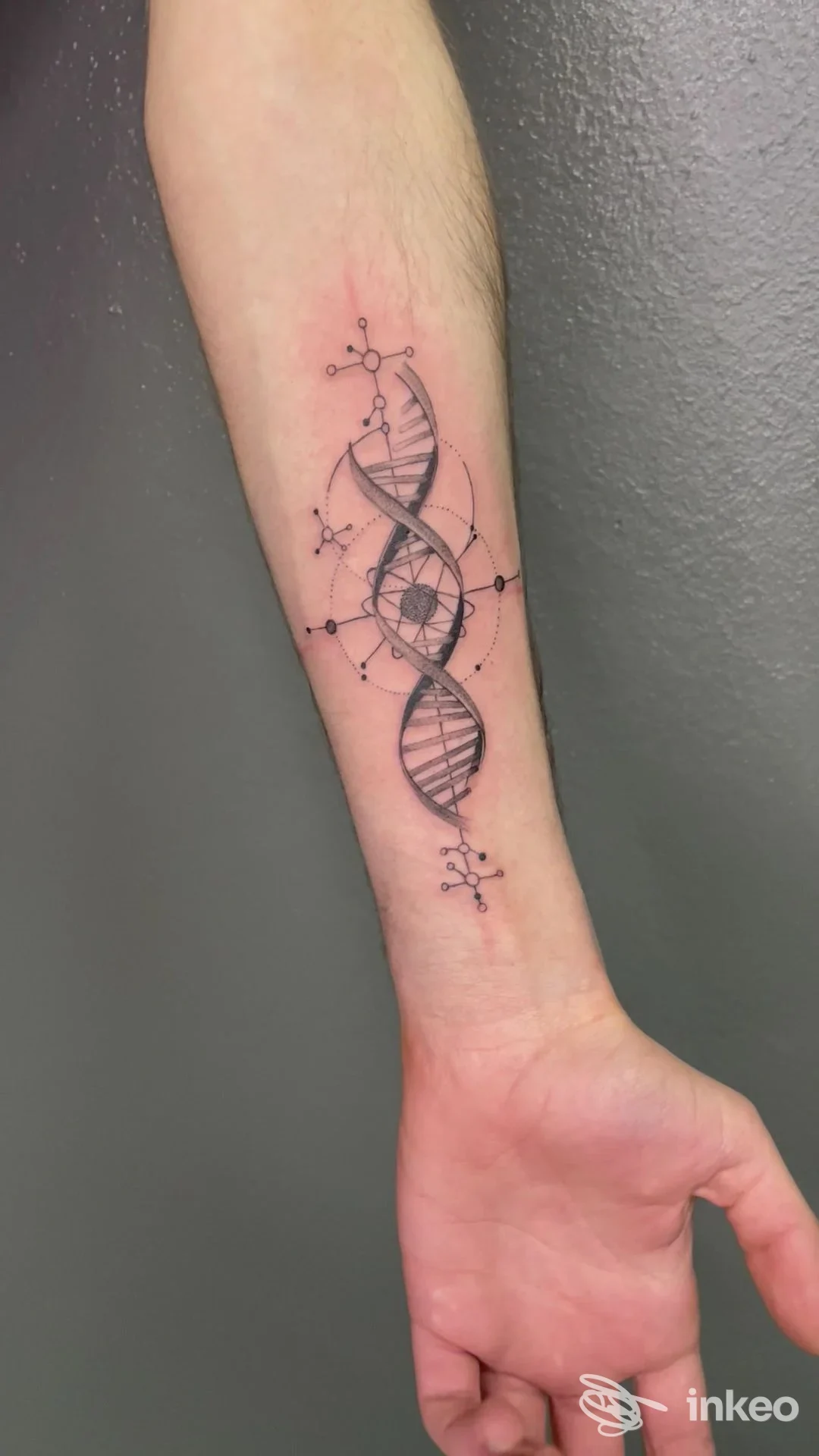Tatuaggio dna a doppia elica sull’avambraccio, con piccole molecole stilizzate intorno, realizzato sulla pelle.