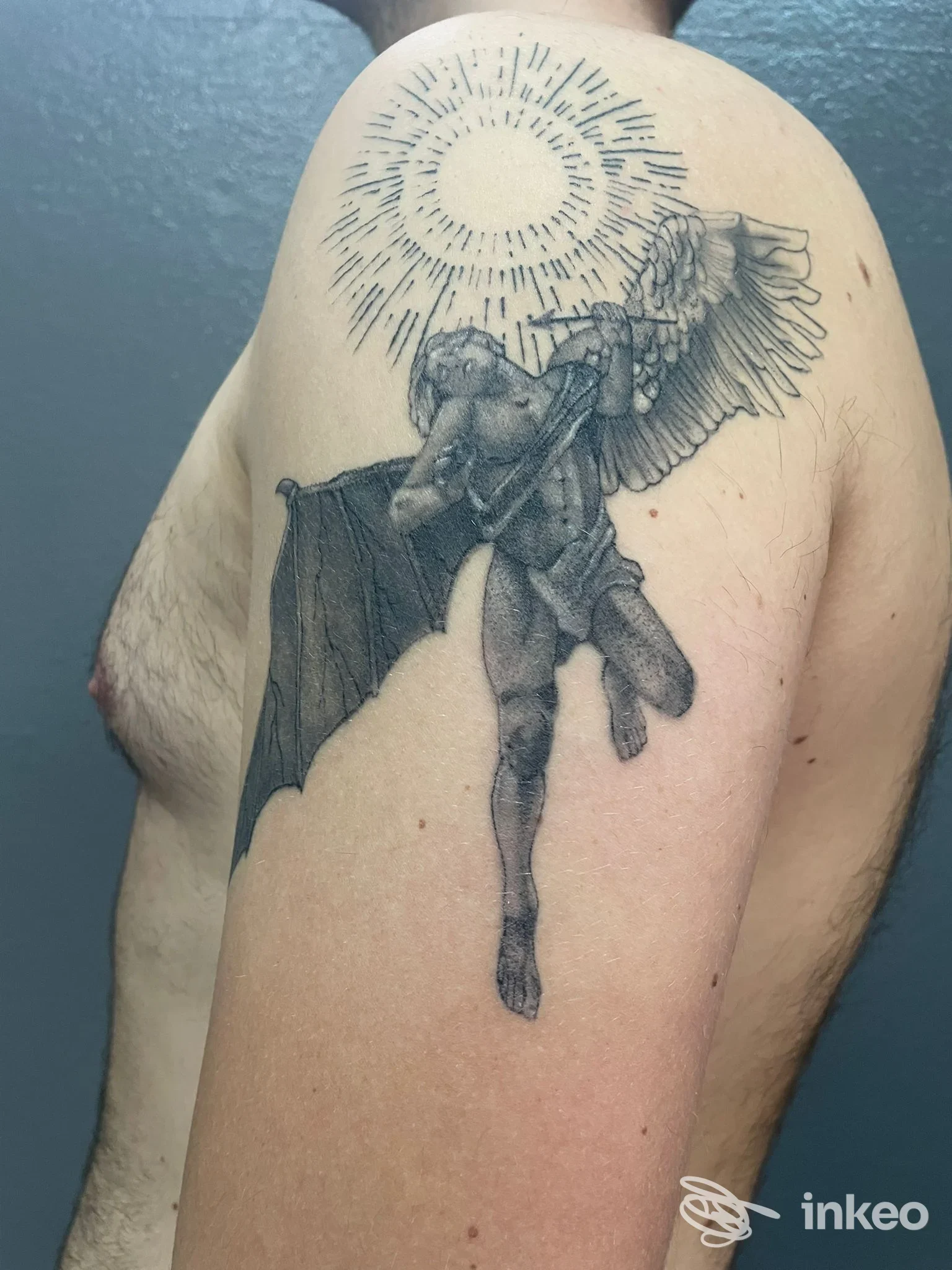 Tattoo realistico di una figura alata con aureola sul dorso della spalla, eseguito sulla pelle di un soggetto.