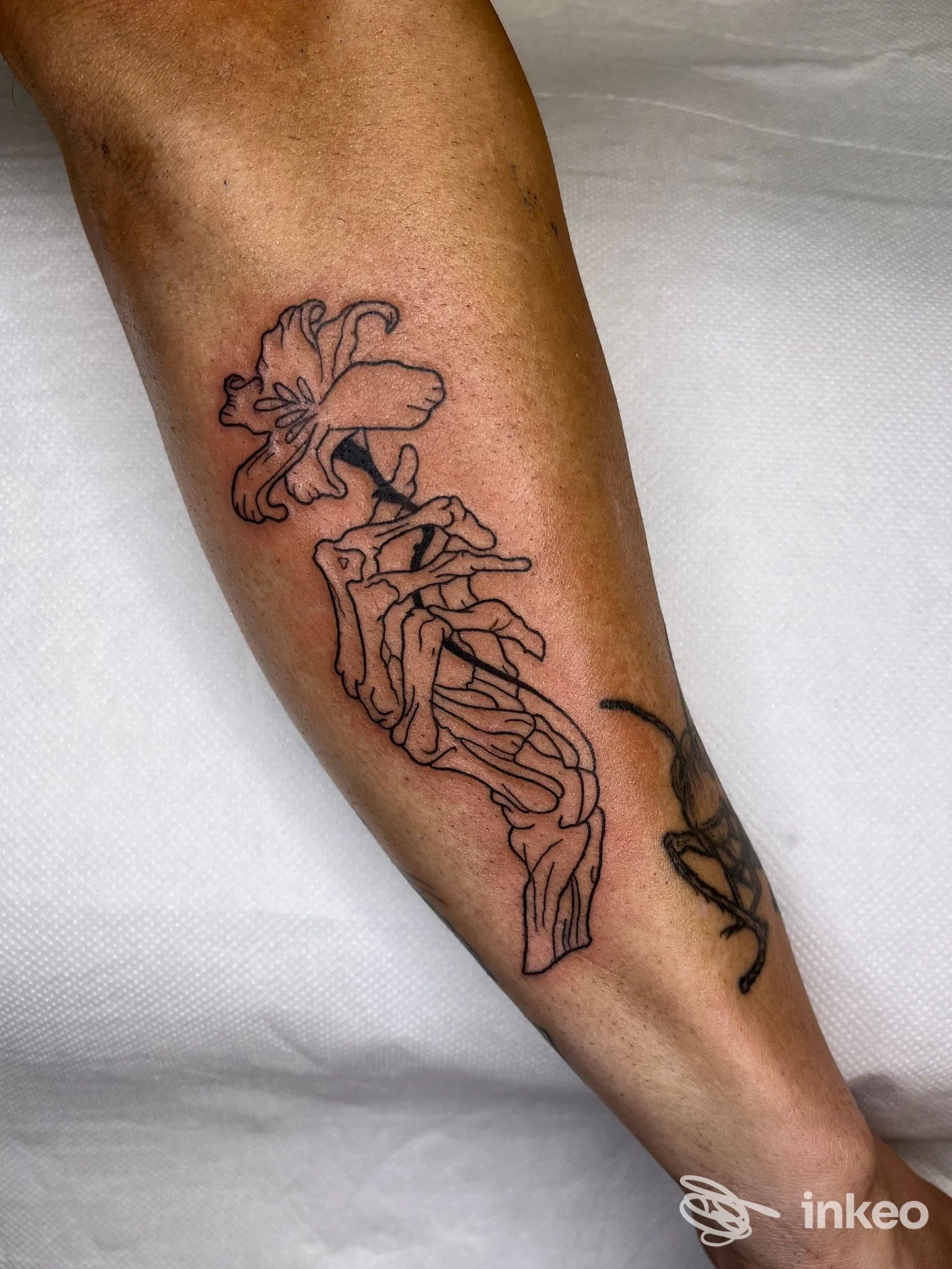 Avambraccio con tatuaggio linework nero a tema floreale e figura scheletrica, foto fornita da Rosegold Tattoo, Chivasso.