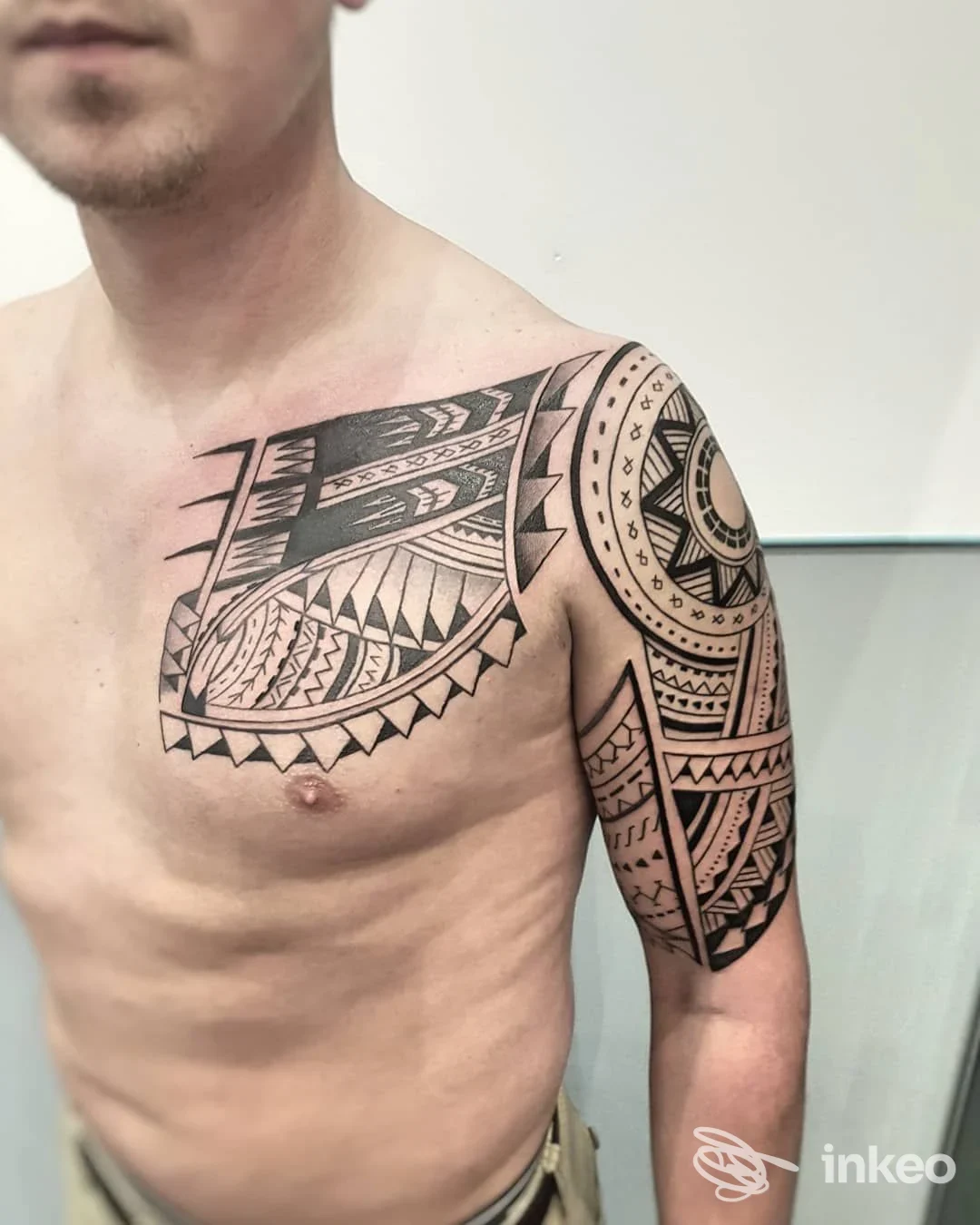 Uomo con ampio tatuaggio a motivi geometrici su petto, spalla e braccio superiore. Prisma Tattoo Studio, Torino.