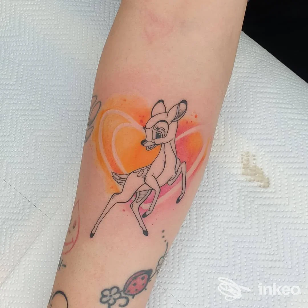 Tatuaggio in stile cartoon di un cerbiatto con sfondo arancione e rosa sull'avambraccio, realizzato presso Red Pant Tattoo & Piercing a Crescentino.