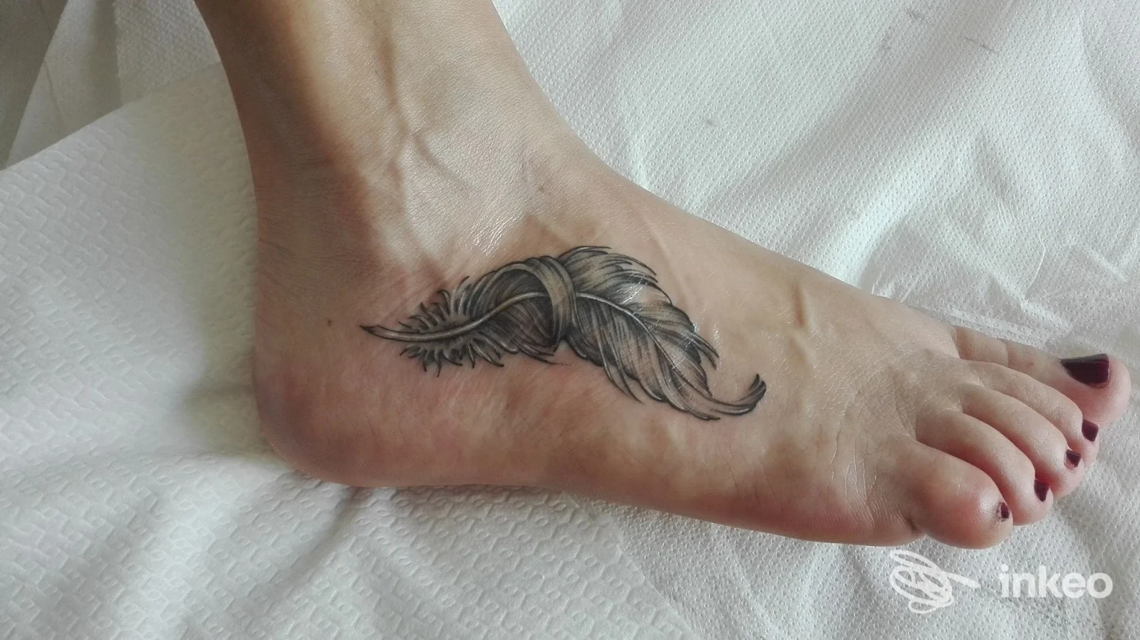 Tatuaggio a forma di piuma in nero e grigio sul lato del piede, fotografato in primo piano: S.M.ART Tattoo Studio, Biella.