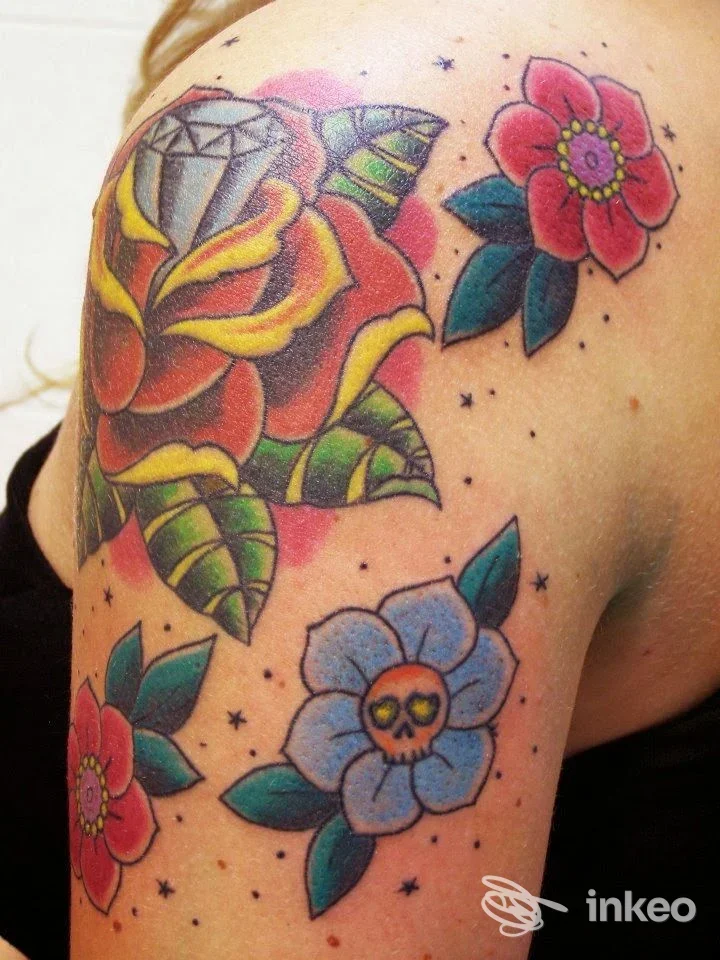 Tatuaggi floreali e colorati sulla spalla e alto braccio, tra cui rosa con diamante e fiore con teschio. Scarlet Skull Studio Tattoo Guglielmo, Moncalieri.
