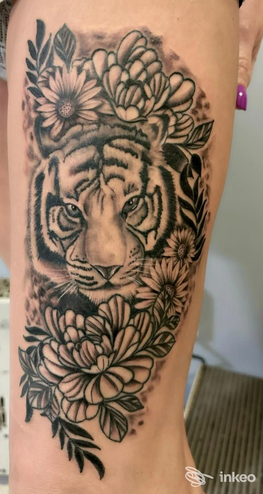 Tatuaggio in bianco e nero di testa di tigre circondata da fiori sul polpaccio, immagine fornita da Skull & Fox Tattoo Studio, Biella.