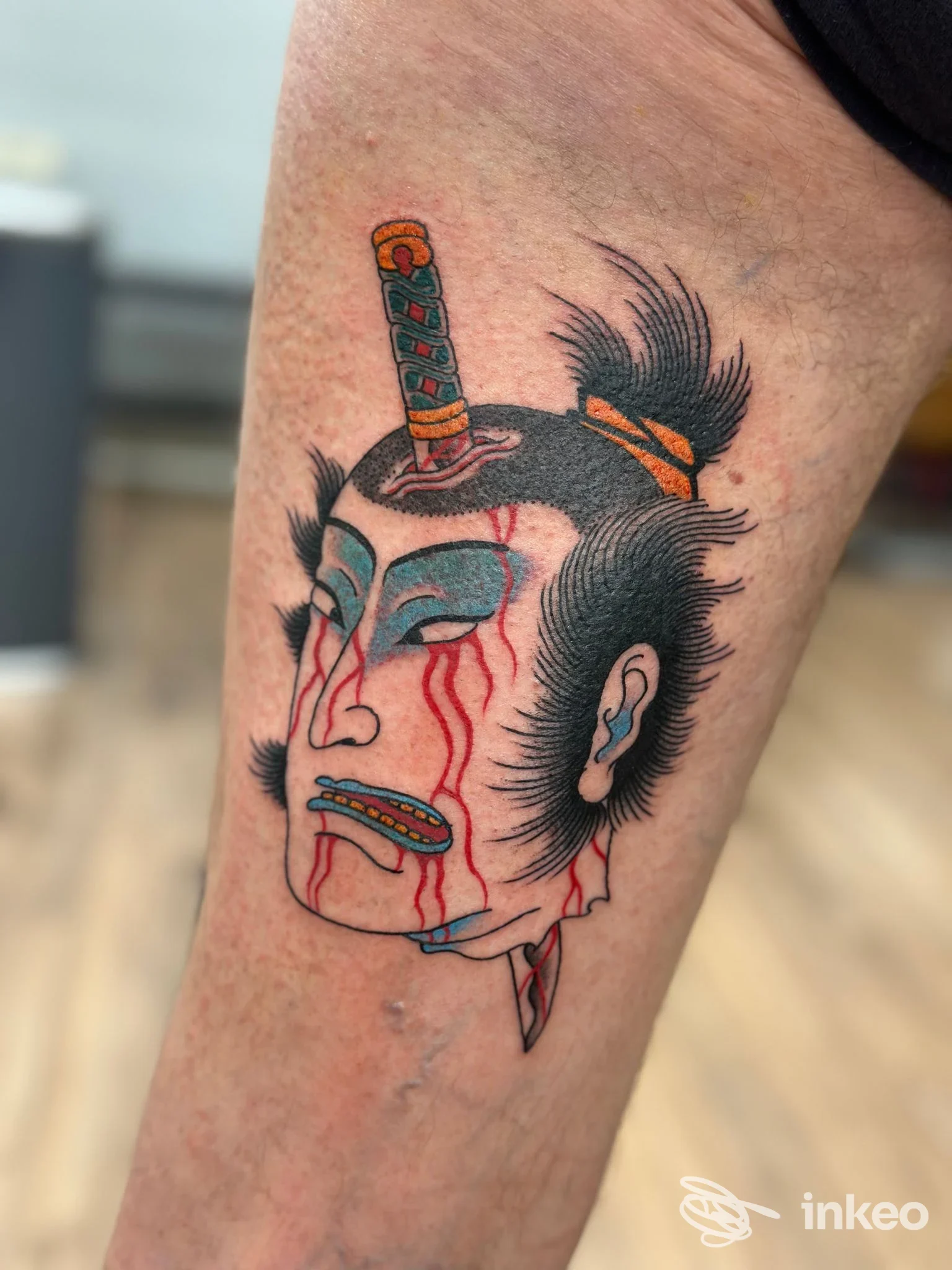 Dettaglio di tatuaggio neo-tradizionale su avambraccio raffigurante una testa con pugnale conficcato e sangue stilizzato. Speakeasy Tattoo Club, Torino.