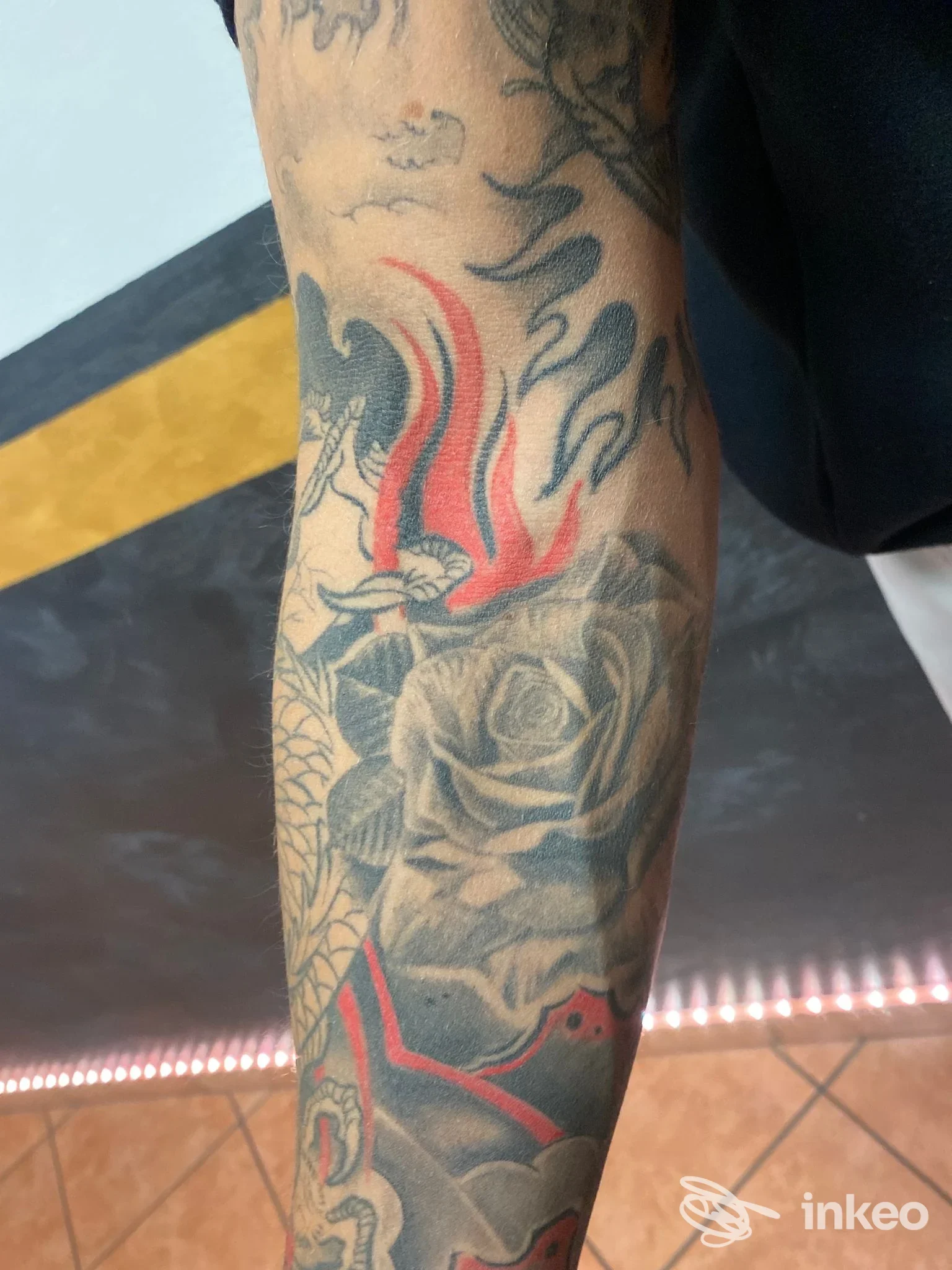 Primo piano di avambraccio tatuato con rosa in bianco/nero e fiamme rosse, foto fornita da SteVi Artist Tattoo, Torino.