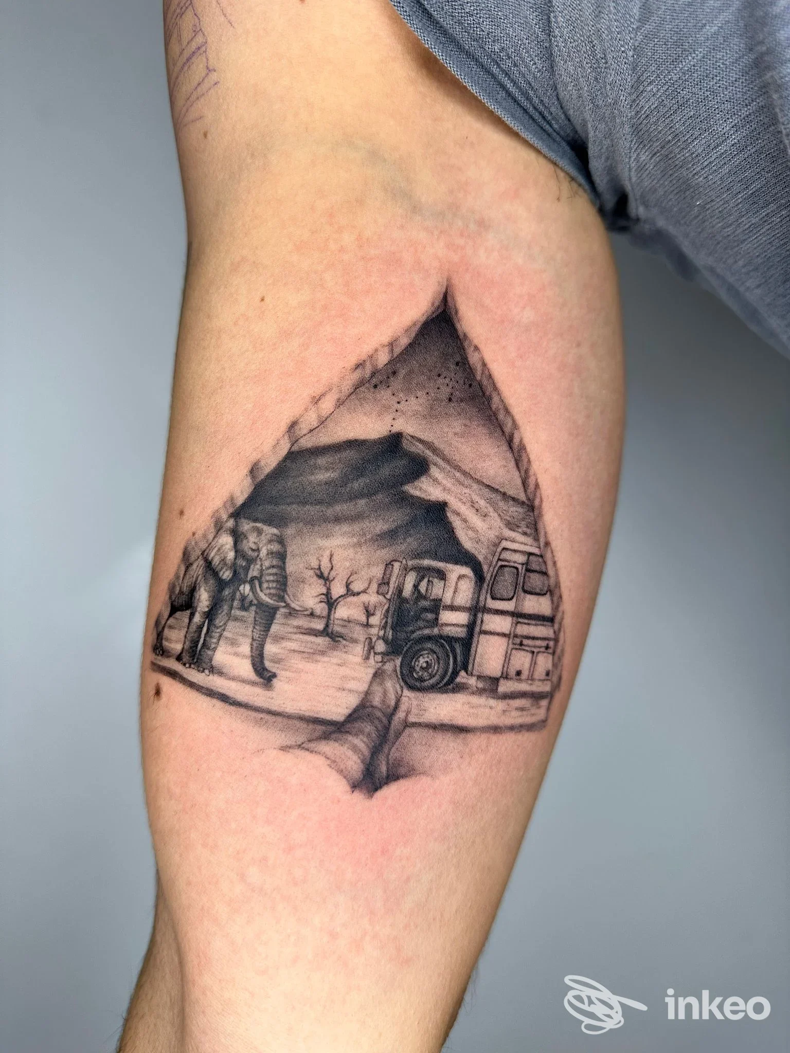 Tattoo raffigurante paesaggio con veicolo e figura umana su braccio, realizzato sulla pelle, senza volto visibile.