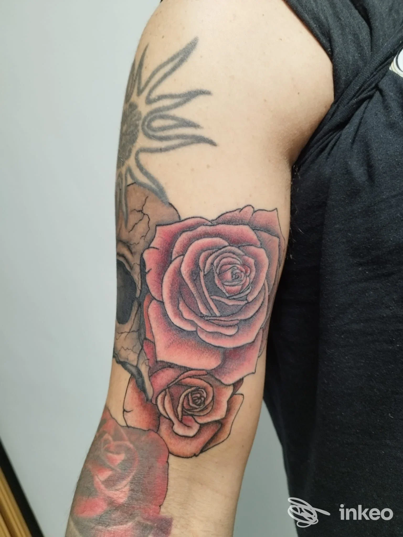 Primo piano del braccio con tatuaggi: rose colorate e teschio in bianco/nero, lavoro fotografato su pelle, Tattoo Studio 220, Ivrea.