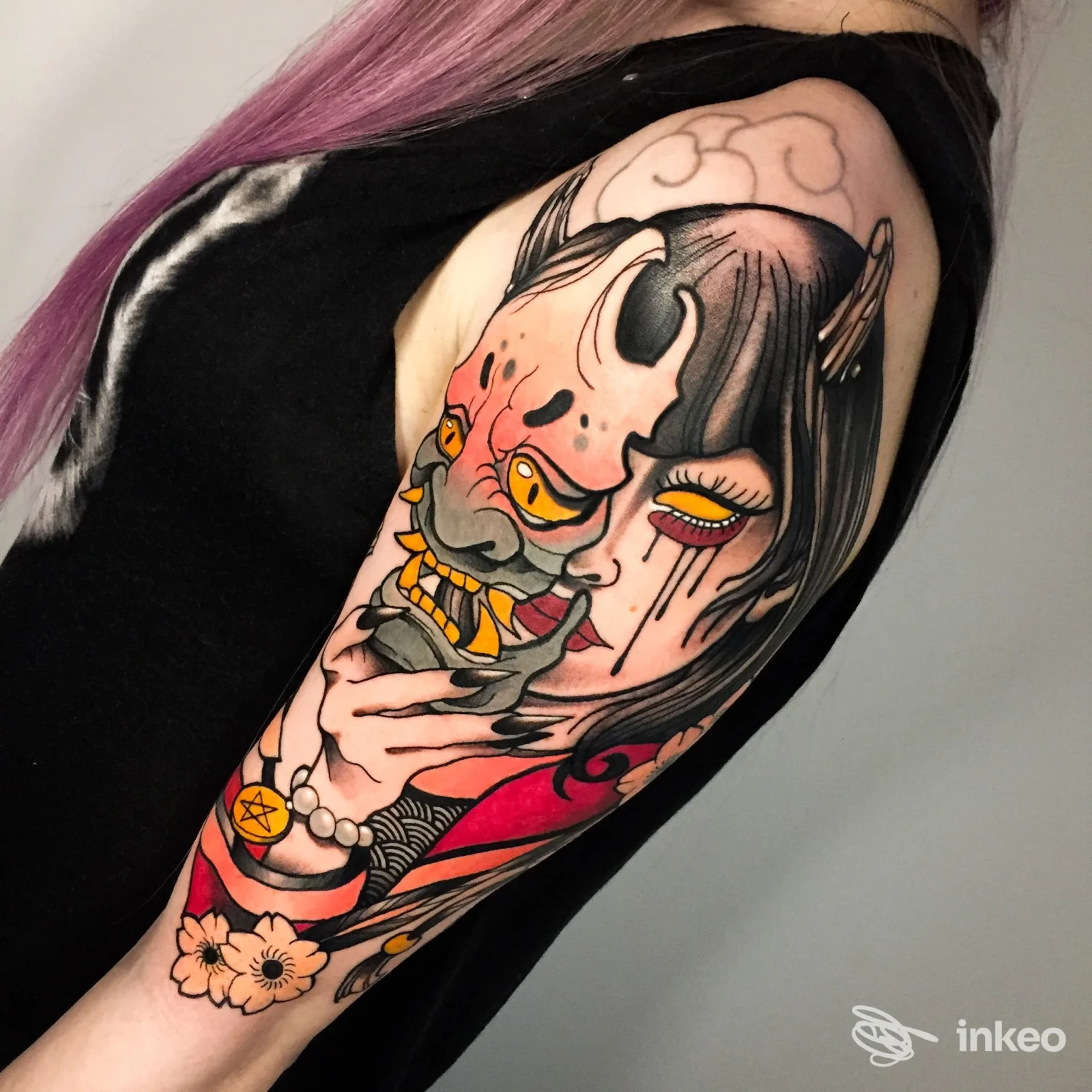 Grande tatuaggio colorato su braccio superiore con volto stilizzato e maschera, foto fornita da Tatuaggi Torino - MENOUNO Studio, Torino.
