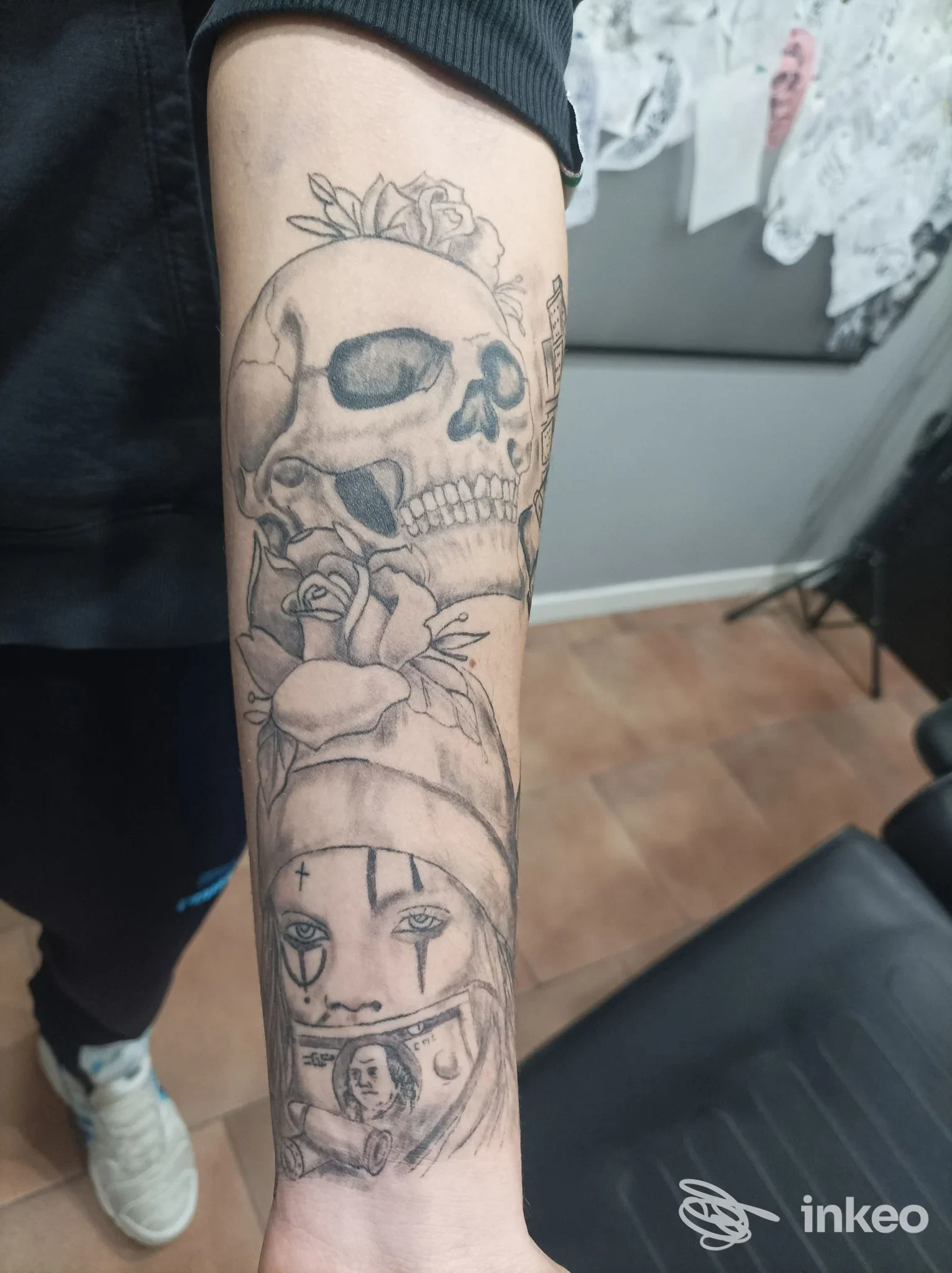 Avambraccio tatuato in bianco e nero con teschio, rose e volto stilizzato, foto fornita da The Saints Tattoo studio a Caselle Torinese.
