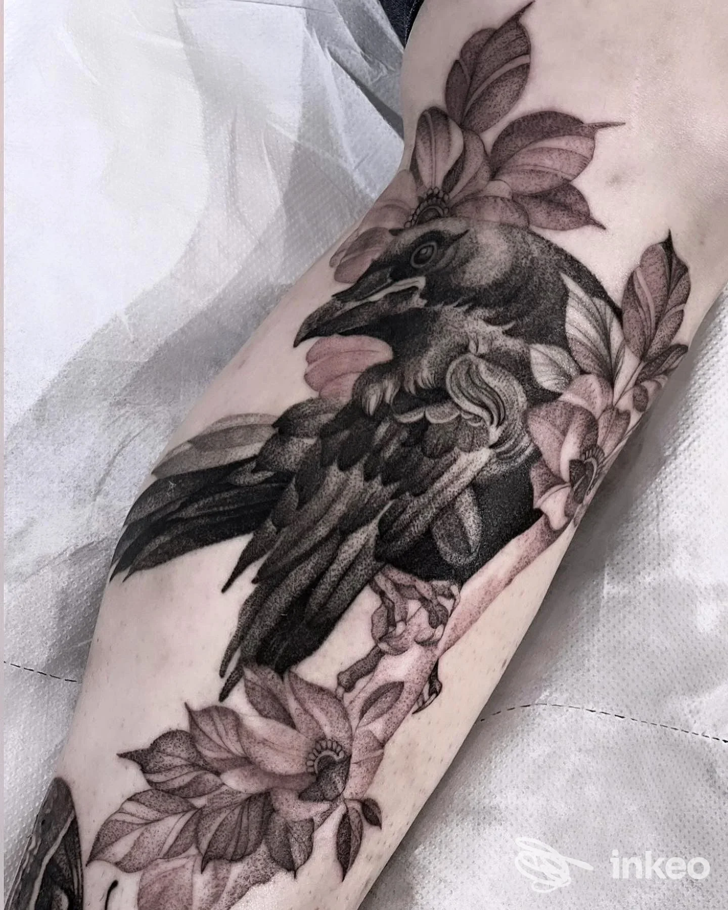 Tatuaggio in bianco e nero di corvo e fiori sull'avambraccio, realizzato da White Raven Tattoo & Art Gallery, Torino.