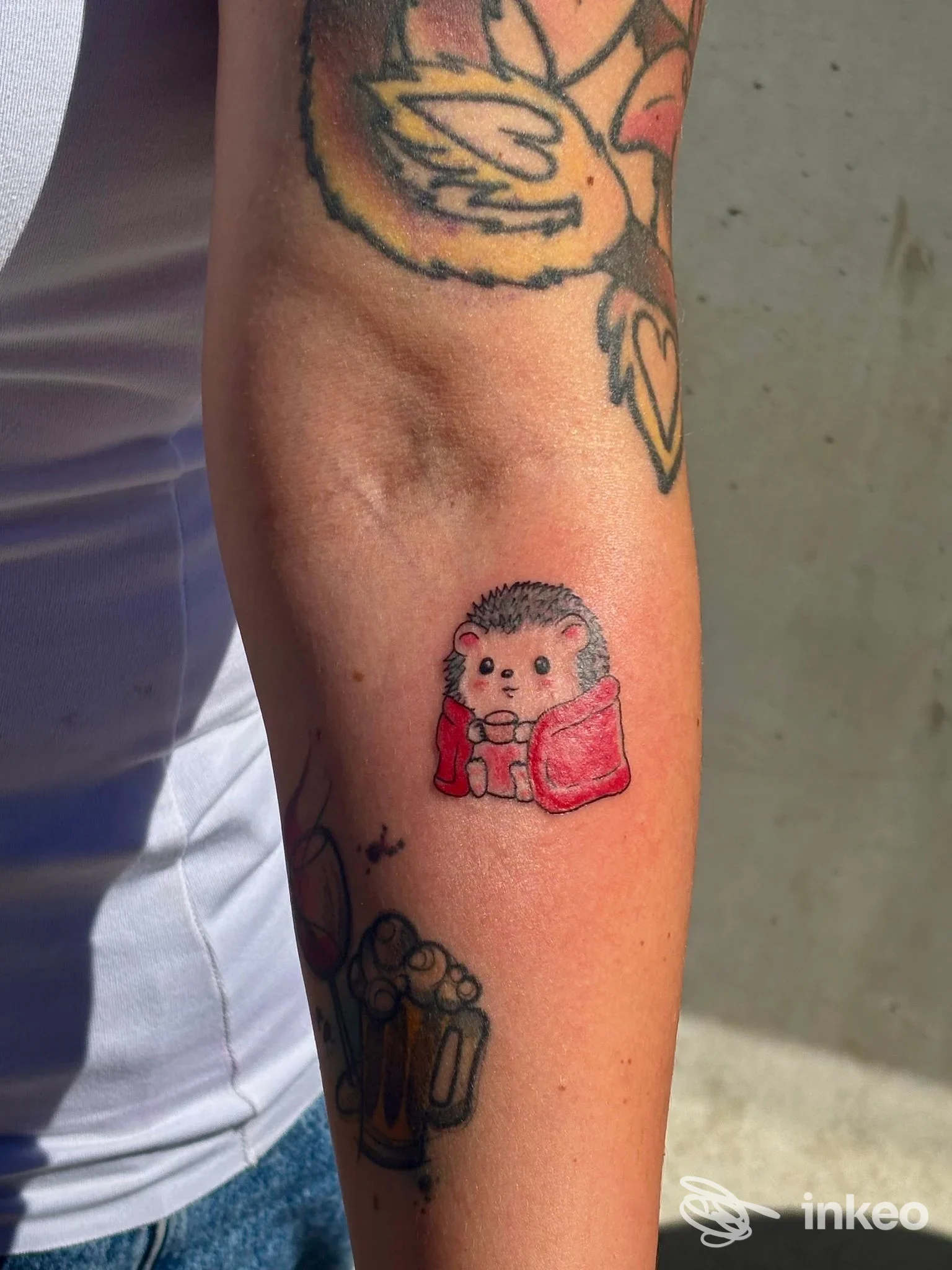 Tatuaggio di un riccio stilizzato con mantello rosso sull'avambraccio, foto realizzata per Yugen tattoo studio Torino.