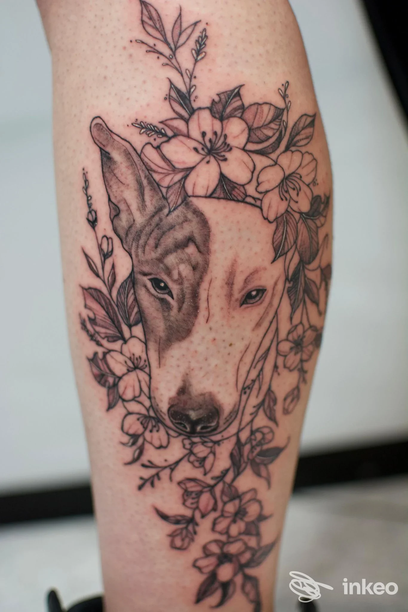 Primo piano di un tatuaggio sul polpaccio con testa di cane circondata da fiori, realizzato da Yugen Tattoo Studio, Torino.
