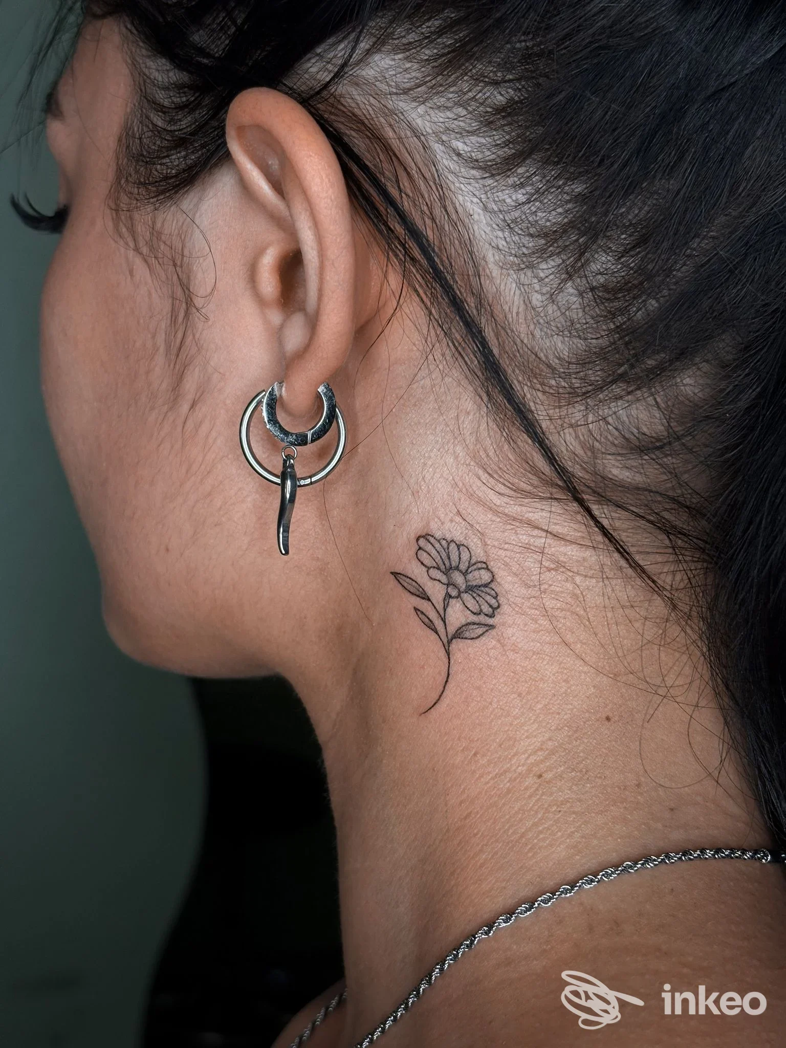 Piccolo tatuaggio floreale in nero sul lato del collo, vicino all'orecchio; immagine per ZANAGA TATTOO, Chivasso.