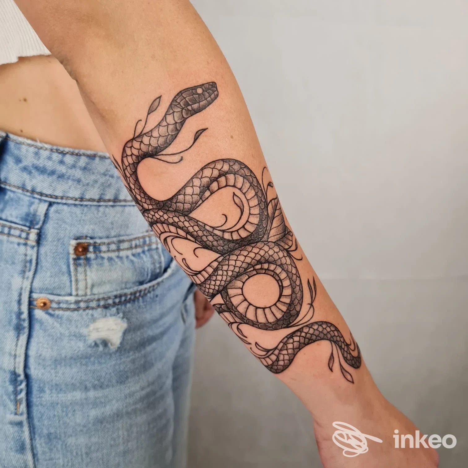 Tattoo su avambraccio: serpente nero che si avvolge lungo la pelle, tratteggio pulito e dettagli di squame, visibile su braccio di una persona.