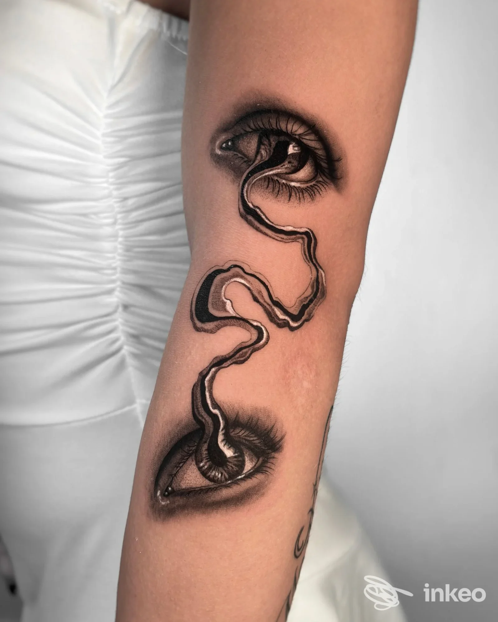 Tatuaggio realistico in bianco e nero con due occhi collegati su avambraccio, Amygdala Tattoo Temple, Biella.