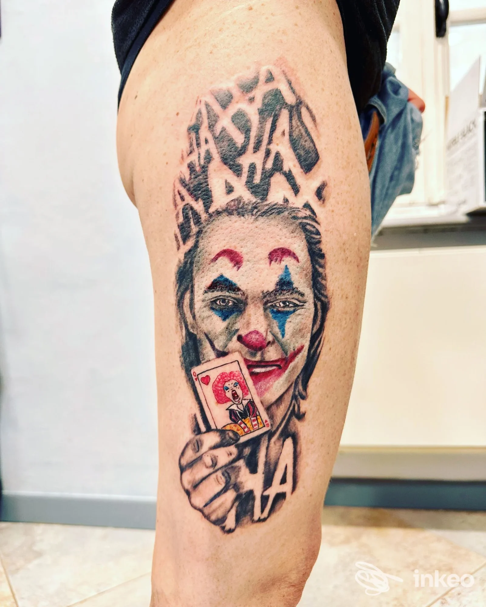 Tatuaggio realistico di volto clown che tiene una carta, su polpaccio. Angeli & Demoni Tattoo Studio, Chieri.