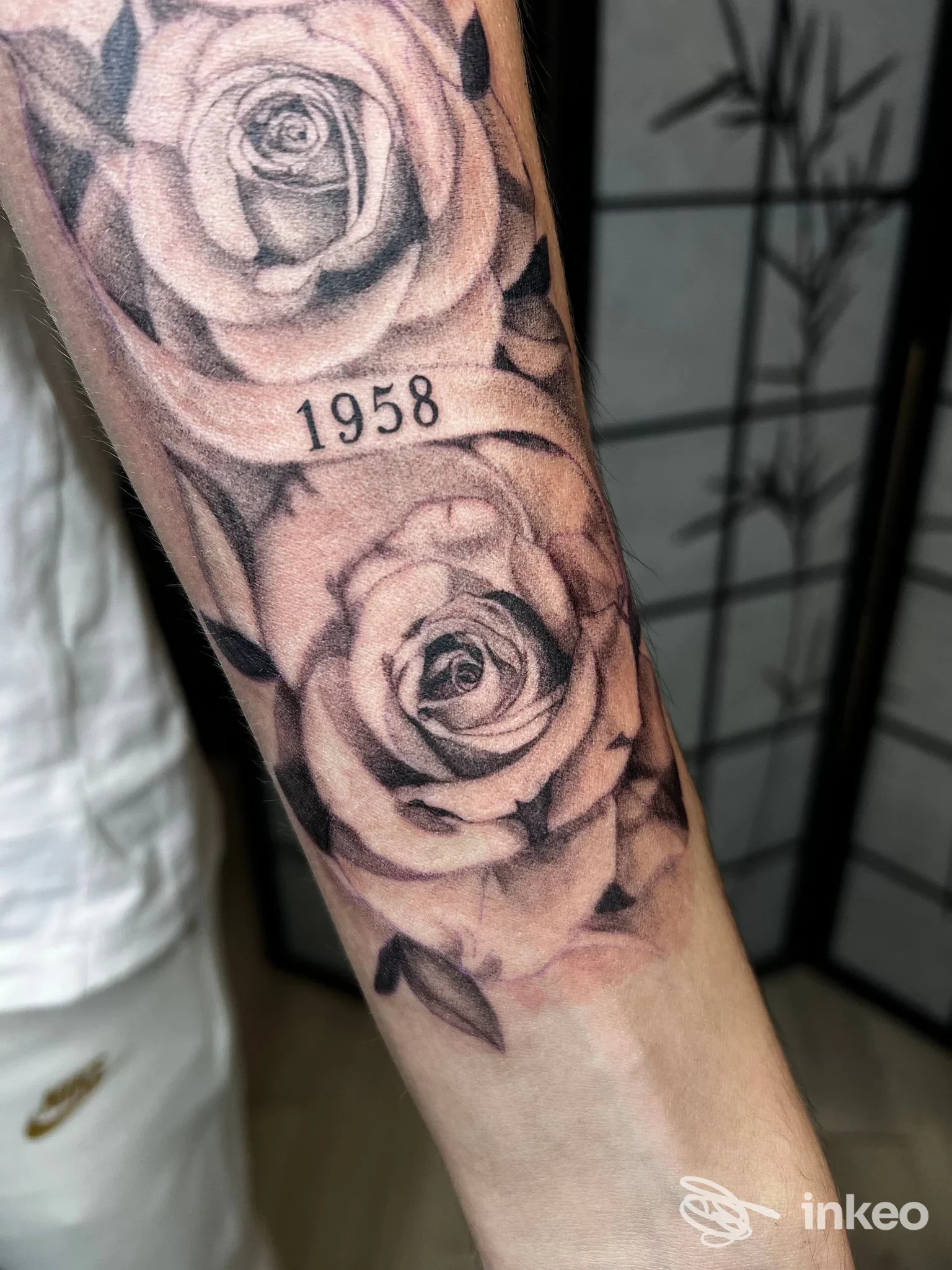 Tatuaggio realistico in bianco e nero di due rose con la cifra '1958' sull'avambraccio, foto fornita da Balam Tattoo Collegno, Collegno.