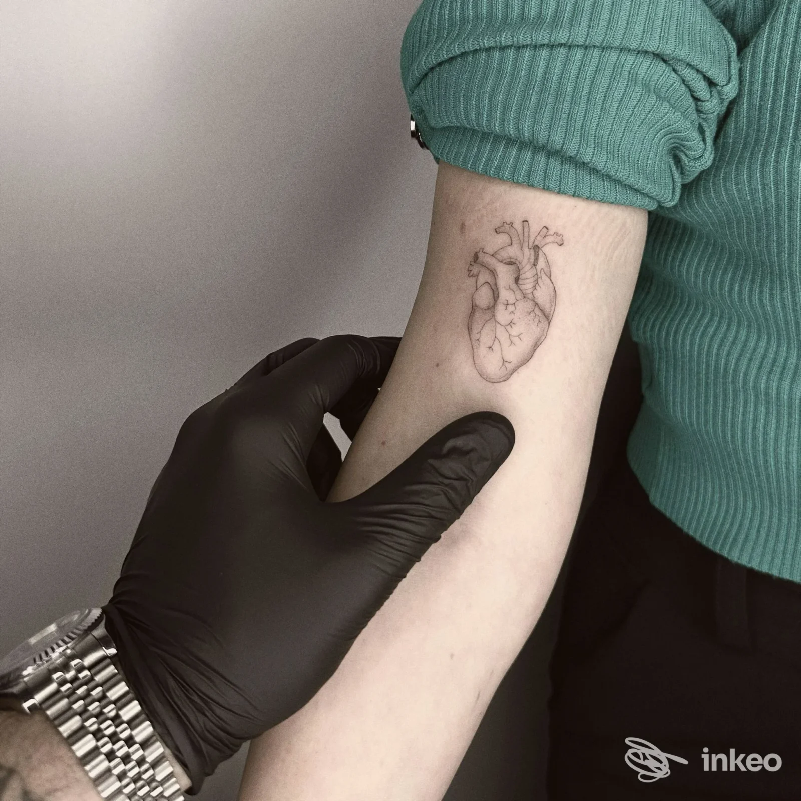 Primo piano di un tatuaggio a linee fini a forma di cuore anatomico sull'avambraccio interno, foto condivisa da Blackout Tattoo Studio, Torino.