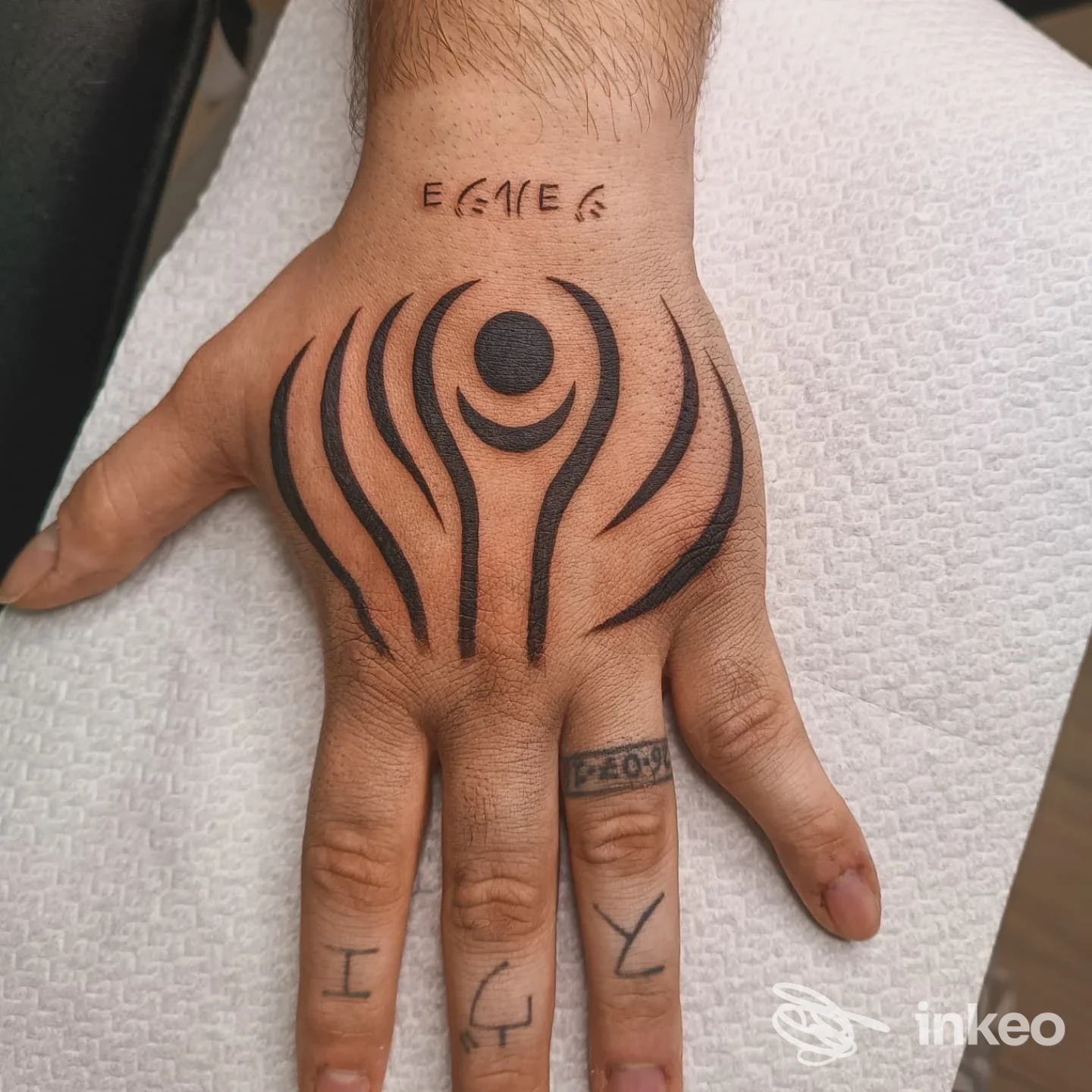 Tattoo sul dorso della mano con motivo astratto nero e cerchio centrale, accompagnato da piccoli tattoo sulle dita, foto singola.