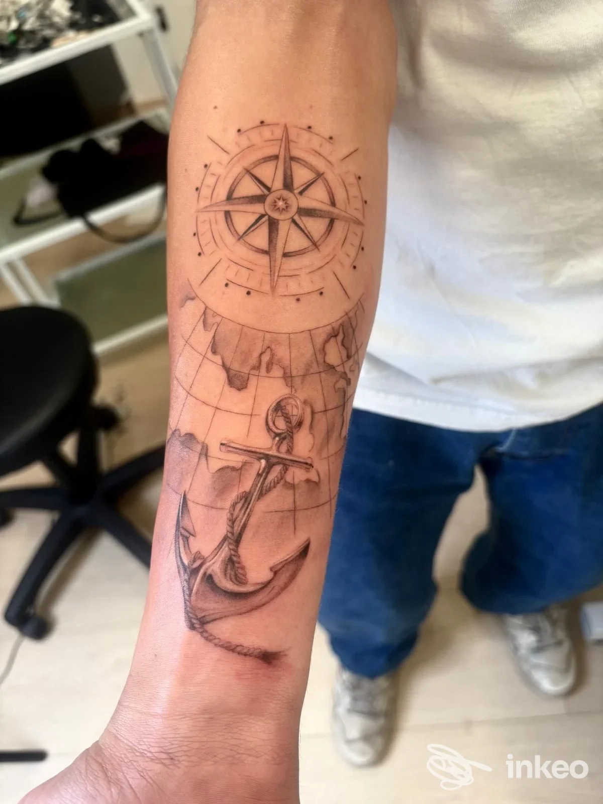 Tattoo sul braccio con bussola stellata sopra e ancora sotto, su sfondo a mappa. Un tema marinaresco su pelle reale.