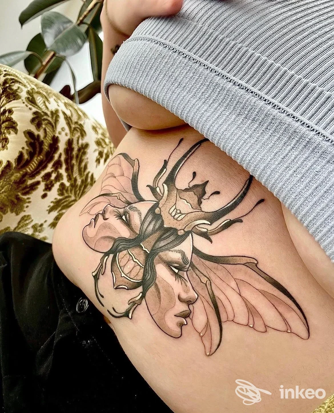 Tatuaggio illustrativo dettagliato sul fianco con due volti fusi e ali d'insetto, su pelle reale. ETRA Tattoo Studio, Torino.