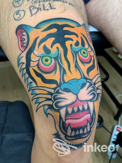 Tatuaggio realistico di tigre colorato sulla pelle del braccio, con rosso e arancione dominante, denti visibili e espressione aggressiva.