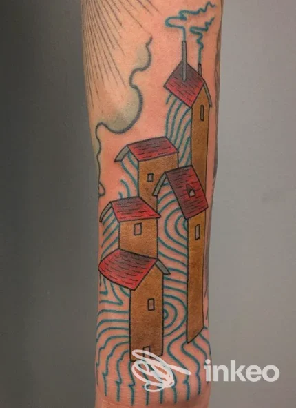 Tattoo su braccio raffigurante case di colori beige con tetti rossi, sfondo a linee azzurre ondulate, senza volto visibile o elementi promozionali.