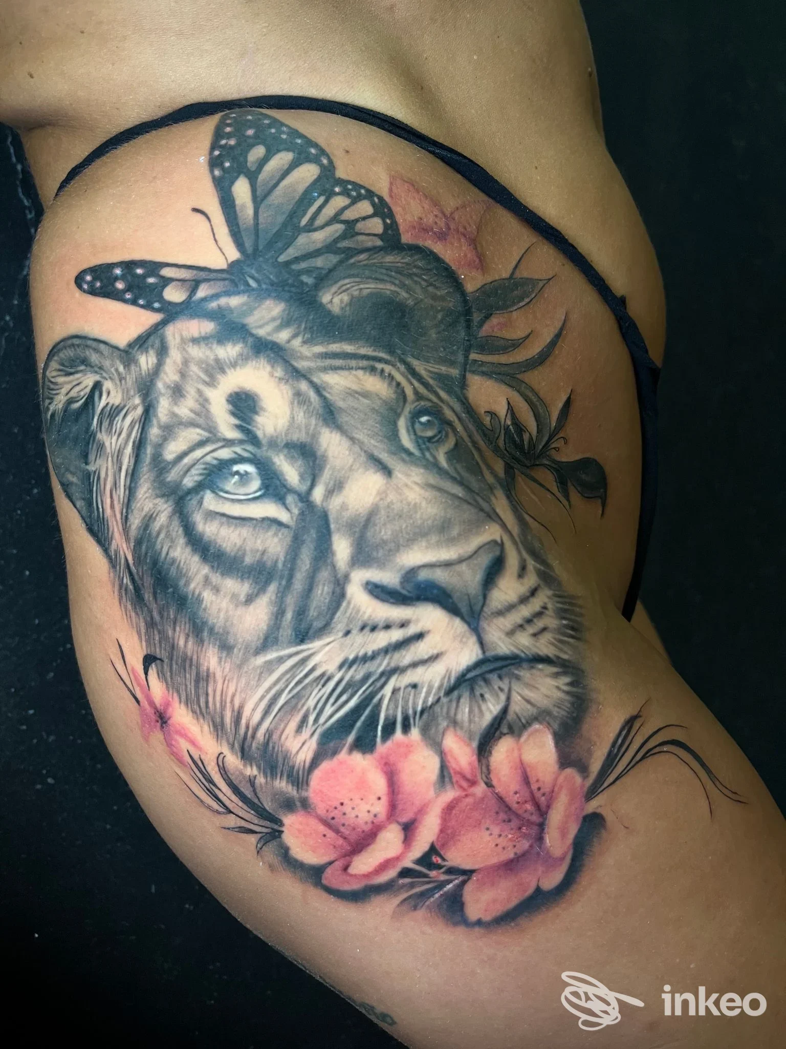 Tatuaggio realistico di leone con farfalla e fiori sul fianco, realizzato da Kingdom Ink Tattoo Studio, Torino.