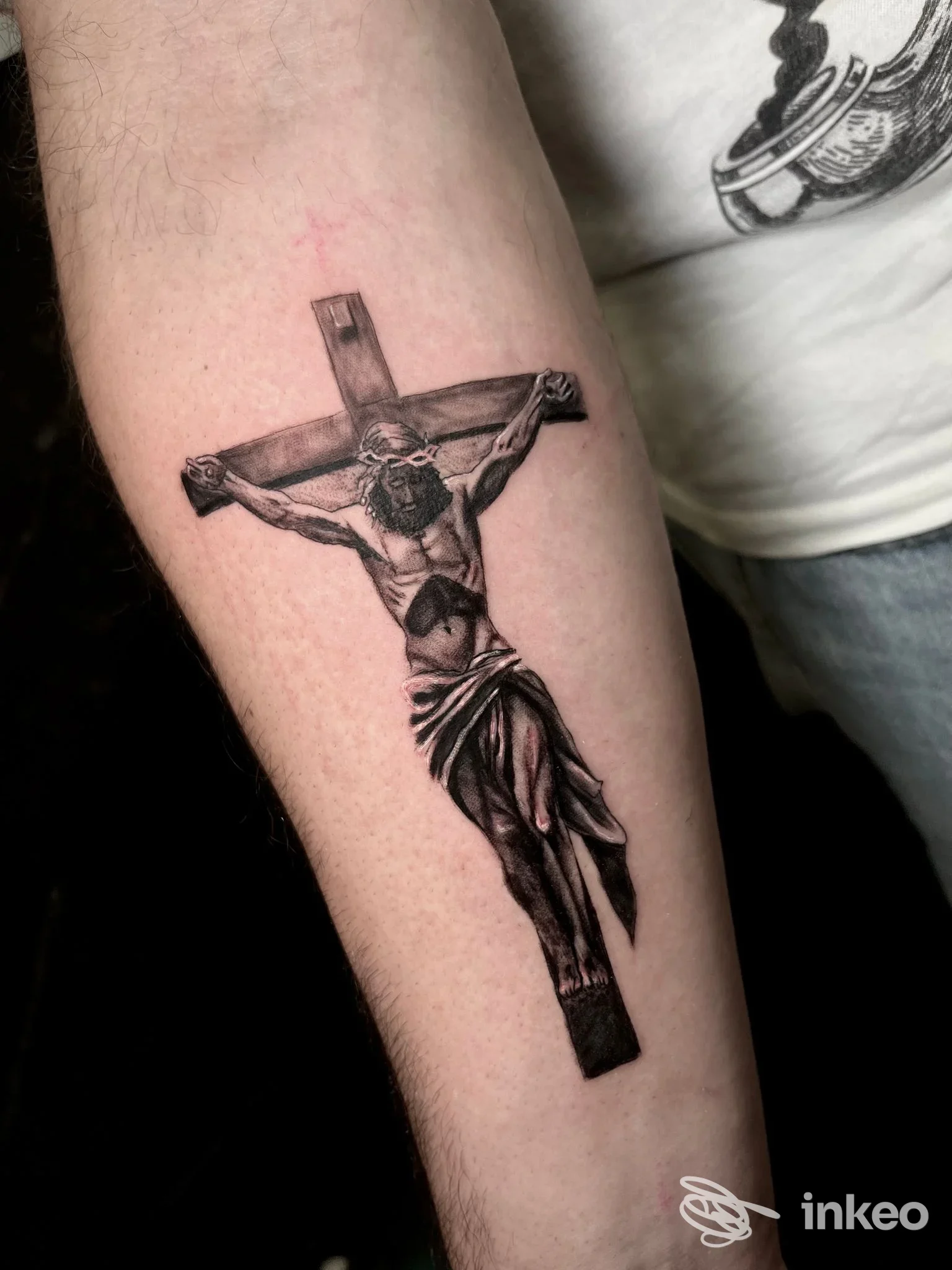 Tatuaggio realistico in bianco e nero di Cristo crocifisso sull'avambraccio, foto fornita da Kingdom Ink Tattoo Studio, Torino.