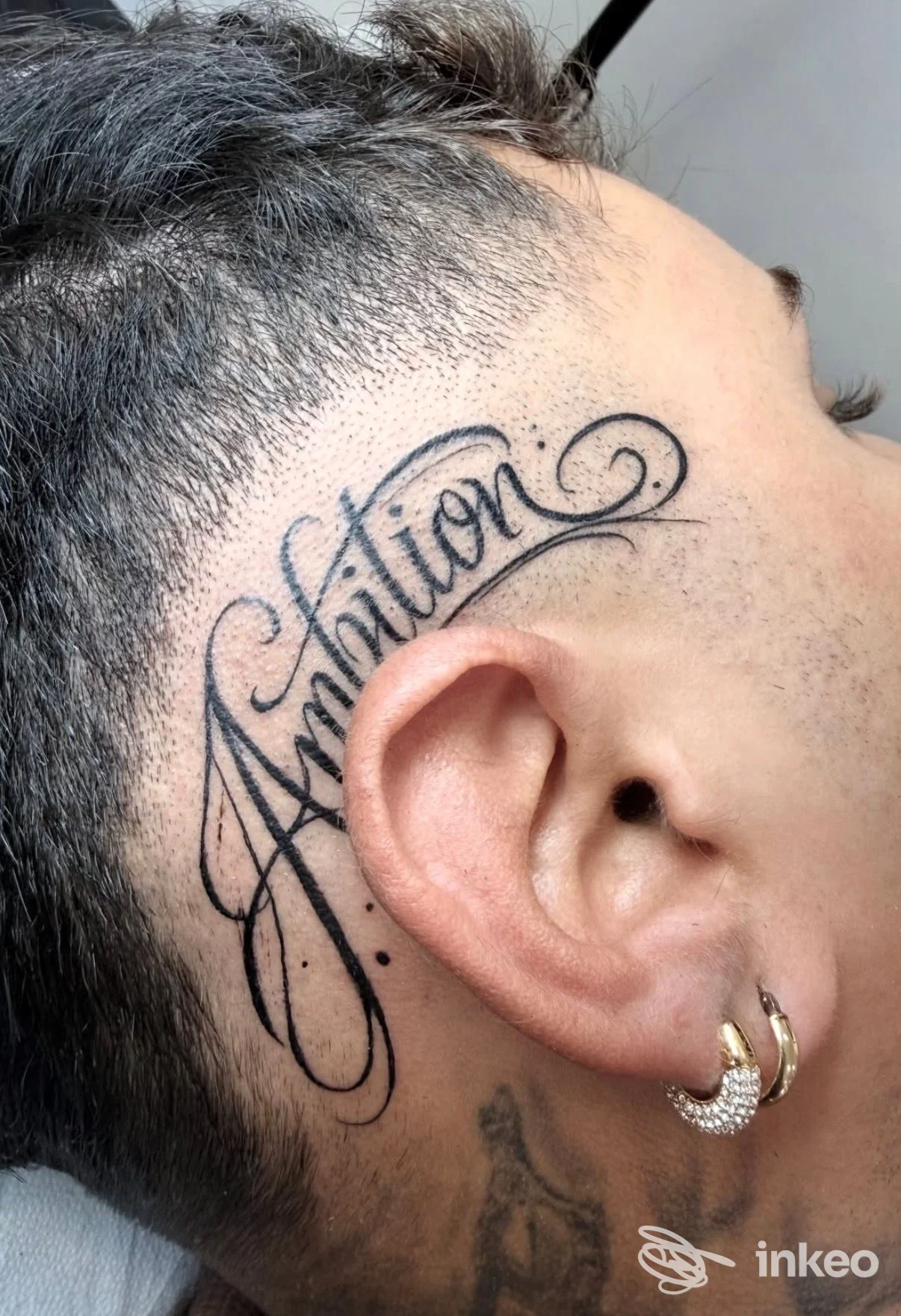 Tatuaggio lettering 'Ambition' sul lato della testa sopra l'orecchio, foto di K-Ink Studio Tattoo a Collegno.