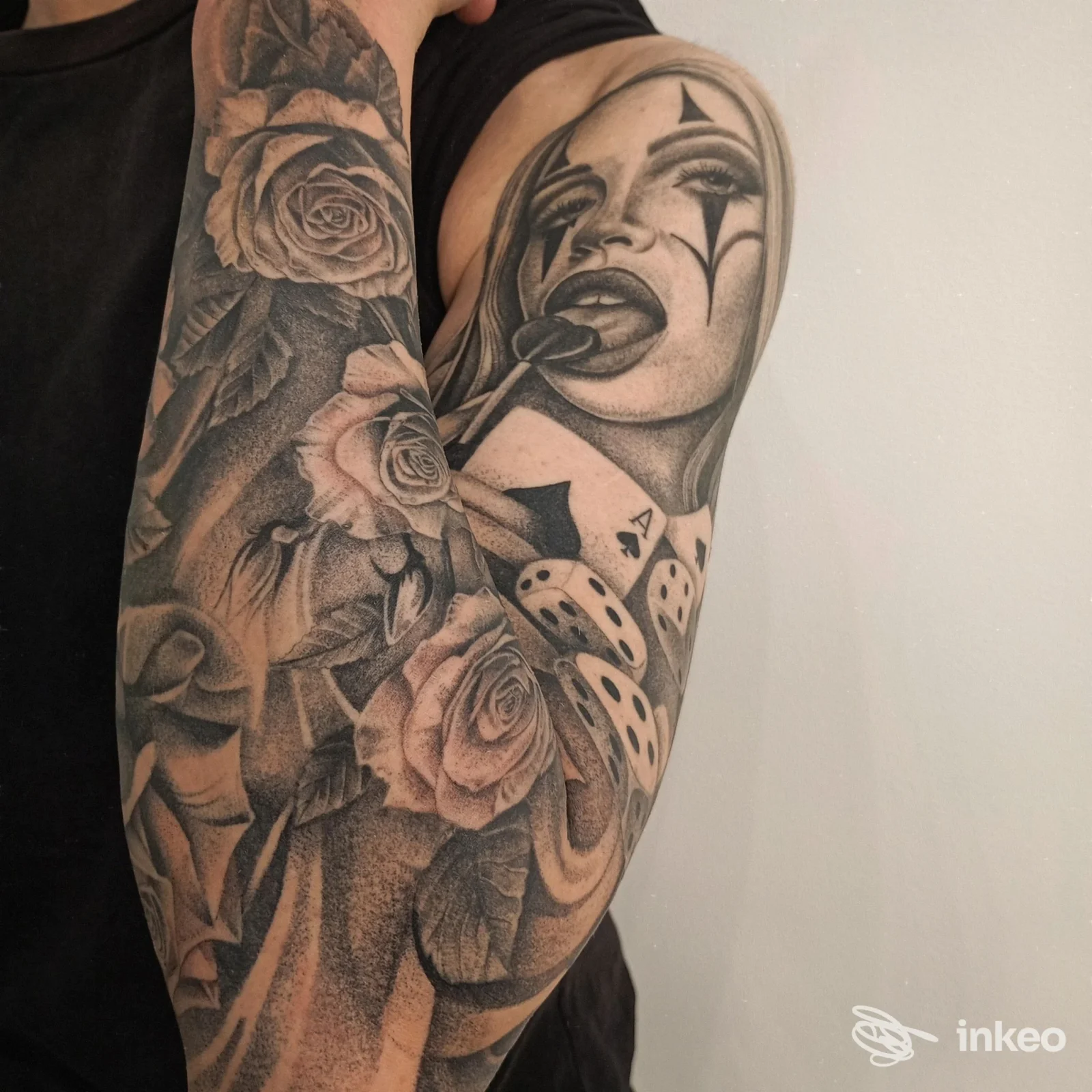 Manica tatuata in bianco e nero con rose dettagliate e un volto stilizzato a clown; immagine fornita dallo studio Kaia Tattoo, Caselle Torinese.