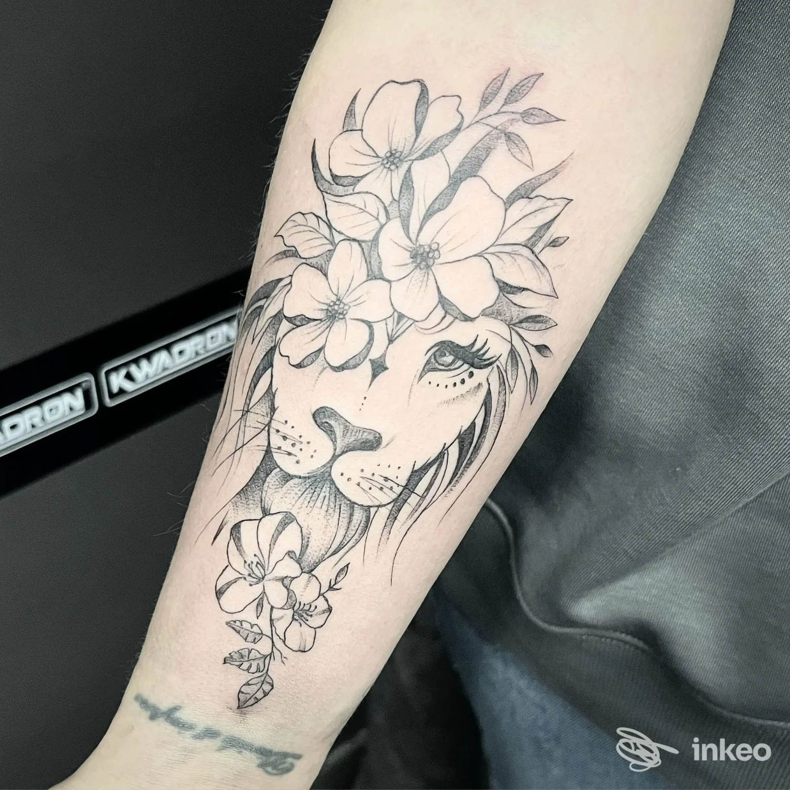 Tatuaggio a inchiostro nero su avambraccio: muso di leone stilizzato con fiori. Inkubus tattoo piercing, Rivarolo Canavese.