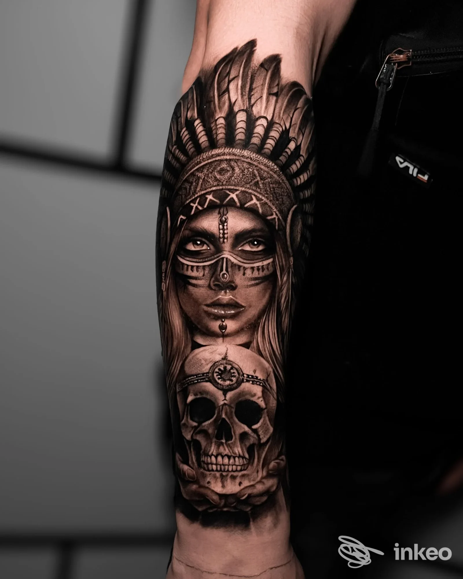 Tatuaggio realistico su avambraccio: ritratto tribale con copricapo piumato e teschio. MINT Tattoo Gallery, Novara.