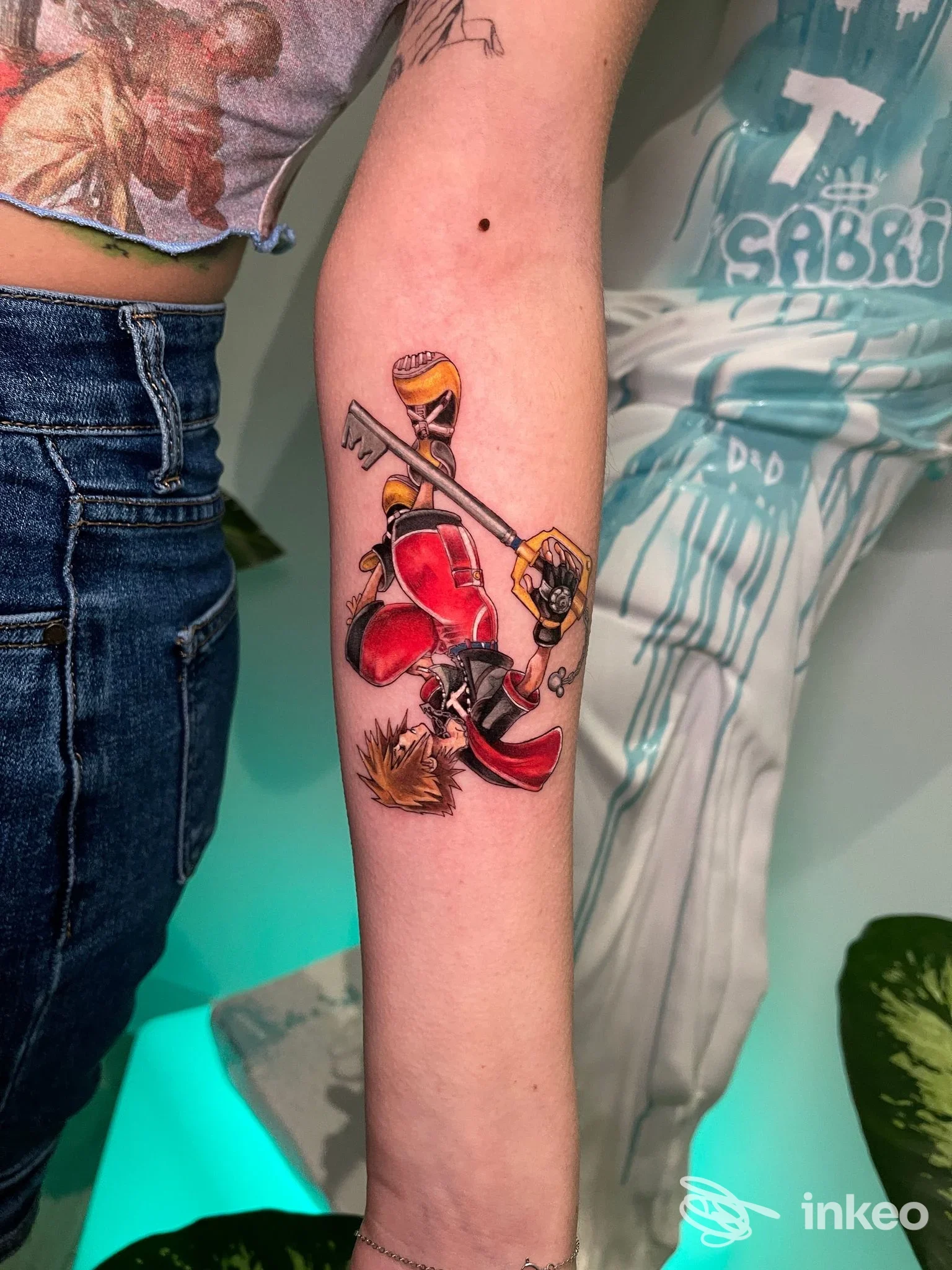 Avambraccio sinistro con tatuaggio colorato raffigurante un personaggio e chiavi, fotografato nello studio MINT Tattoo Gallery a Novara con luce controllata.