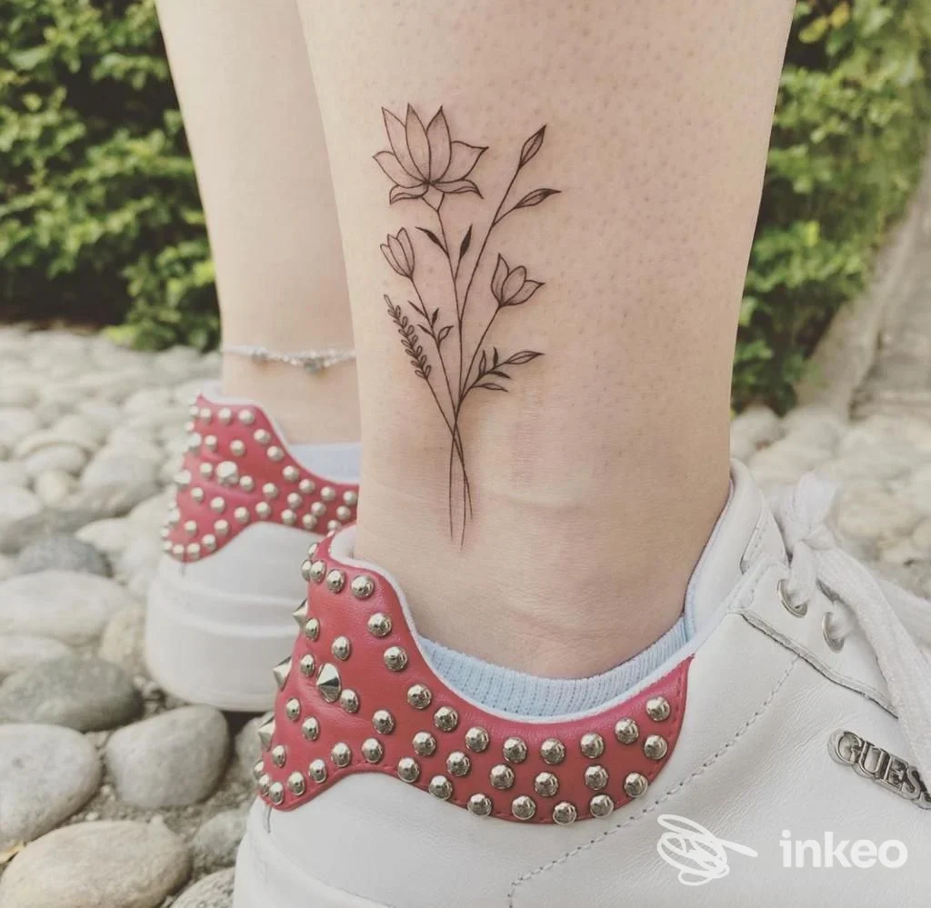 Tatuaggio minimalista a inchiostro nero con fiori sulla caviglia, realizzato da Oonà TATTOO a Torino.