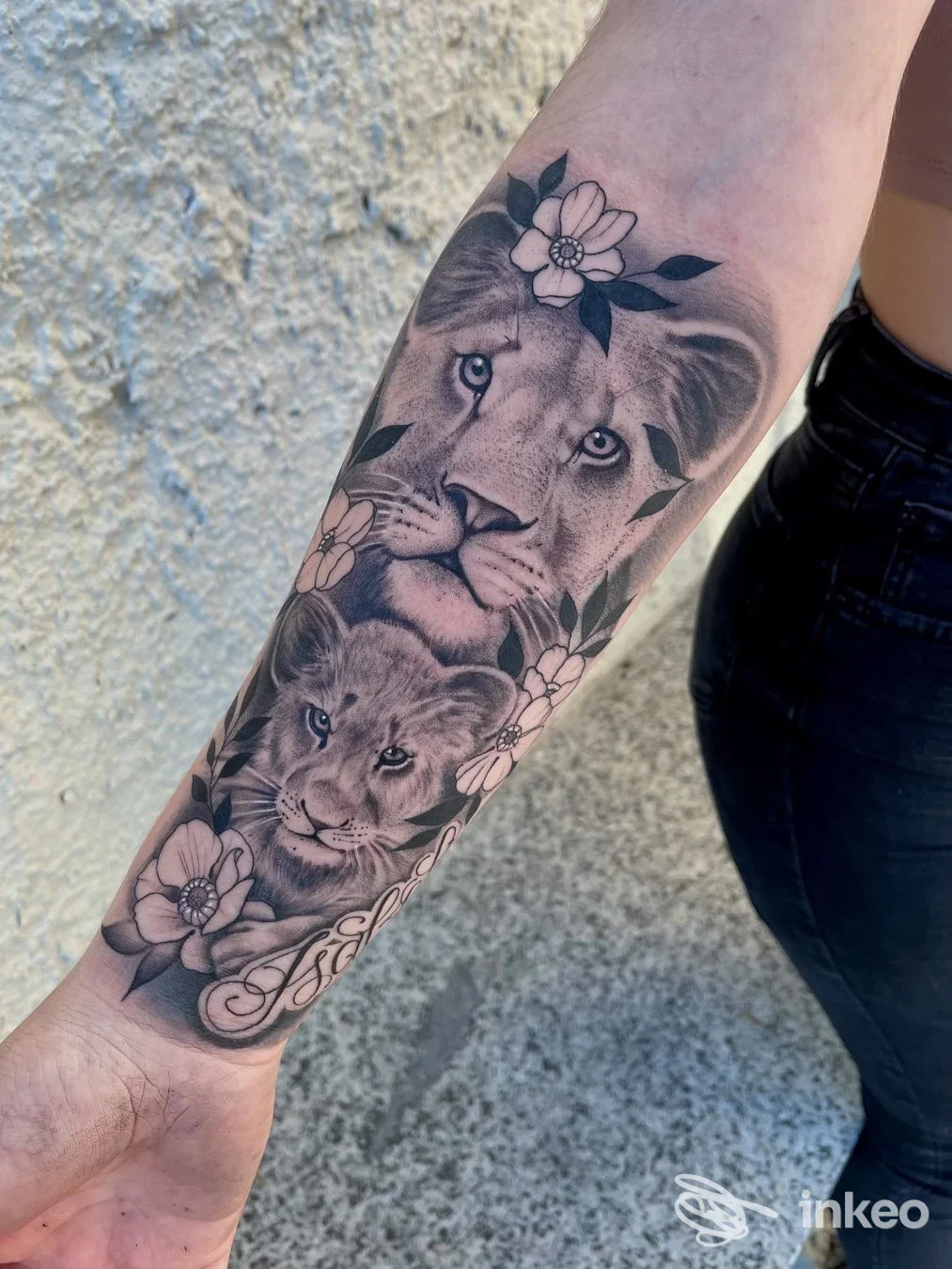 Tatuaggio realistico di due leoni con fiori sull'avambraccio, foto inviata dallo studio SIMOHOLY quality Tattoo&Piercing a Viverone.